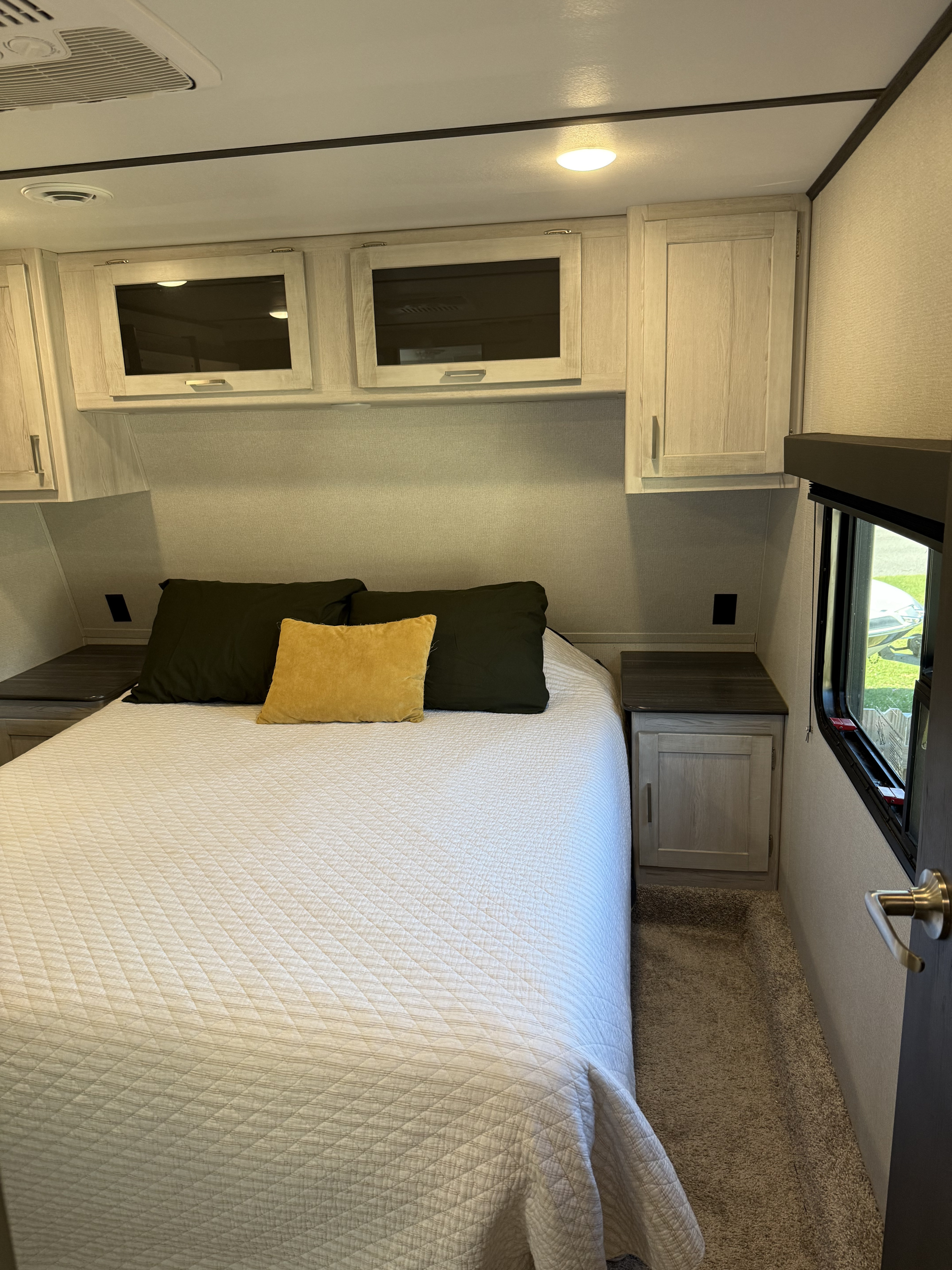 Cozy RV rental bedroom featuring a quilted bed, overhead cabinets, and a nightstand with a window view.. Keystone RV Sprinter Campfire 2021