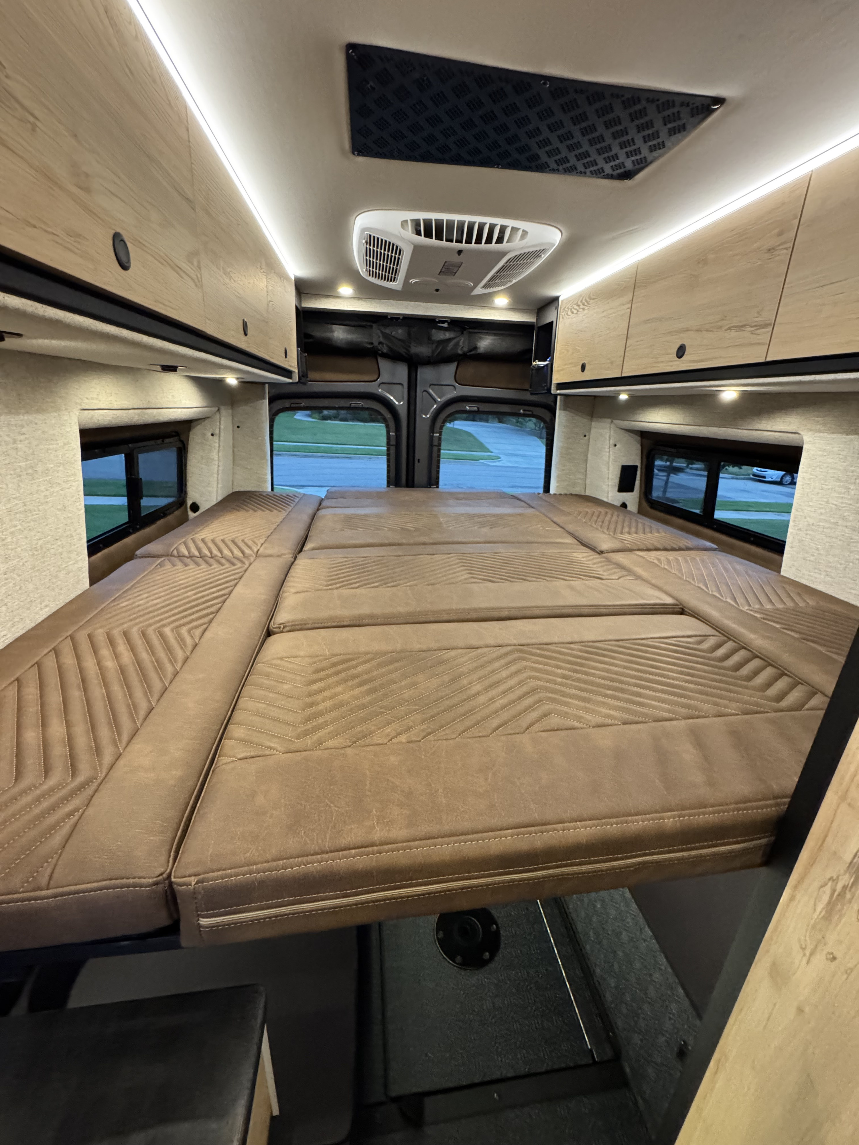 Inside an rv rental: plush bed with geometric stitching, overhead cabinets, and bright lighting for a cozy travel experience.. Storyteller Overland Crew Mode XL 2025