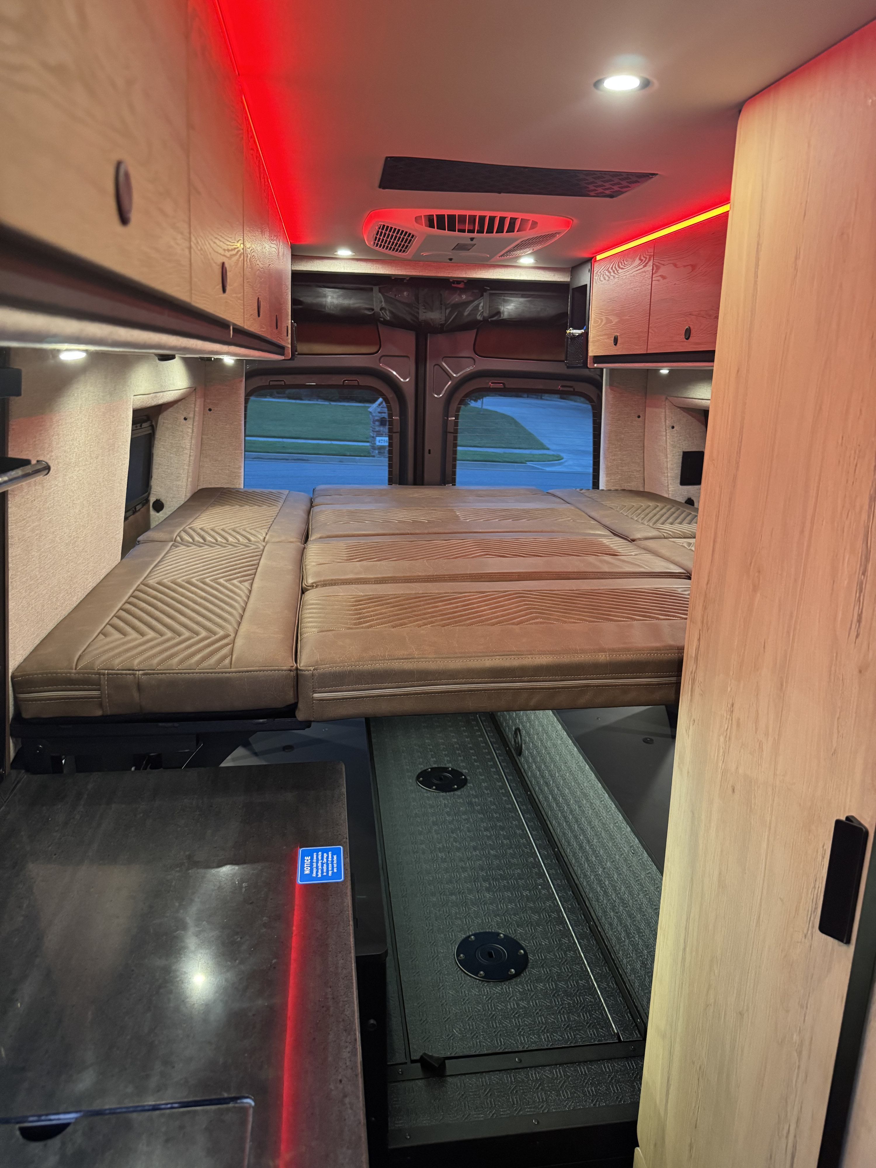 Cozy RV rental interior featuring a plush bed, overhead cabinets, and ambient red lighting for comfortable mobile living.. Storyteller Overland Crew Mode XL 2025