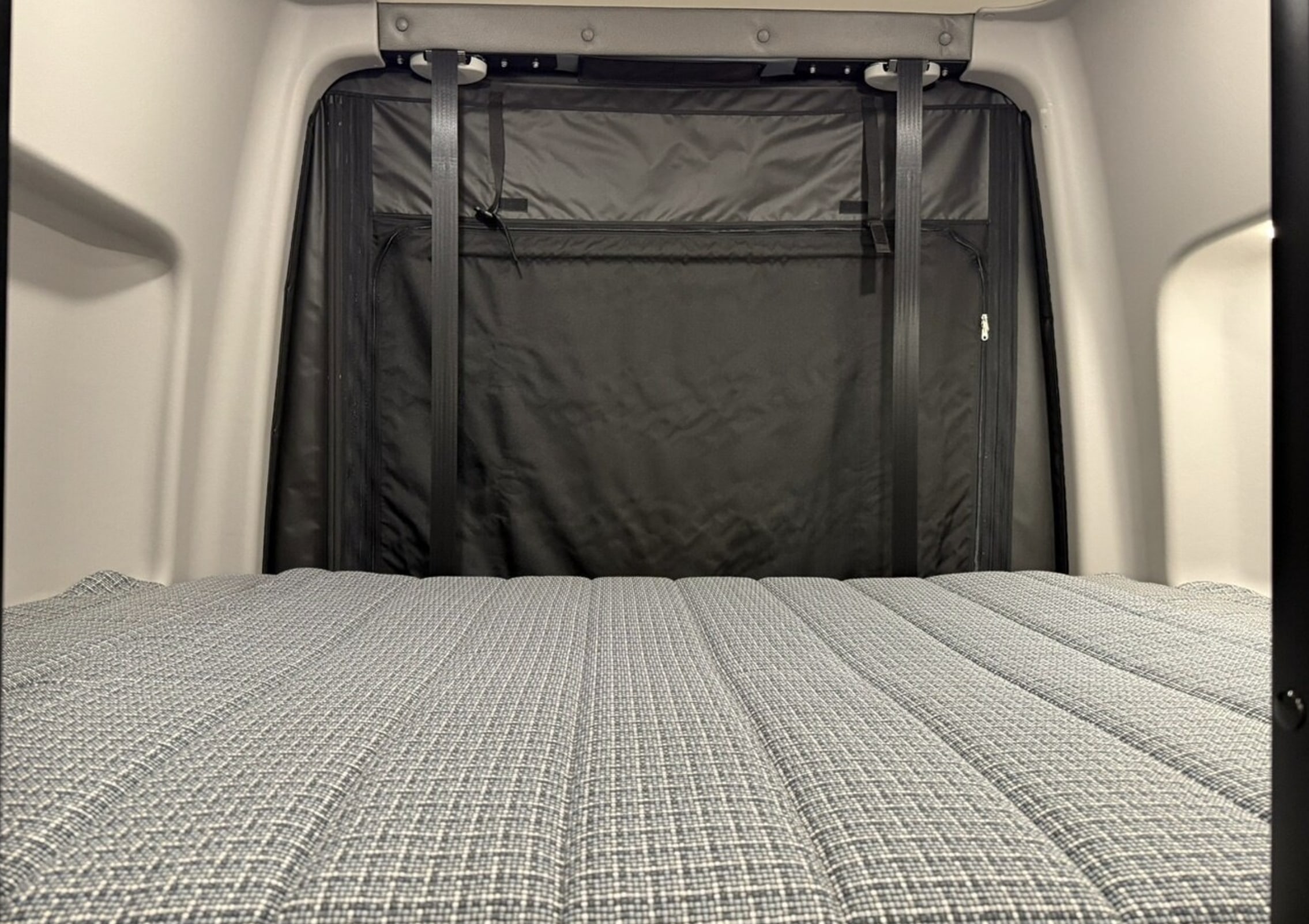 RV rental: View of a comfortable camper van bed with a grey patterned mattress and a black privacy/storage screen.. Winnebago Revel 2024