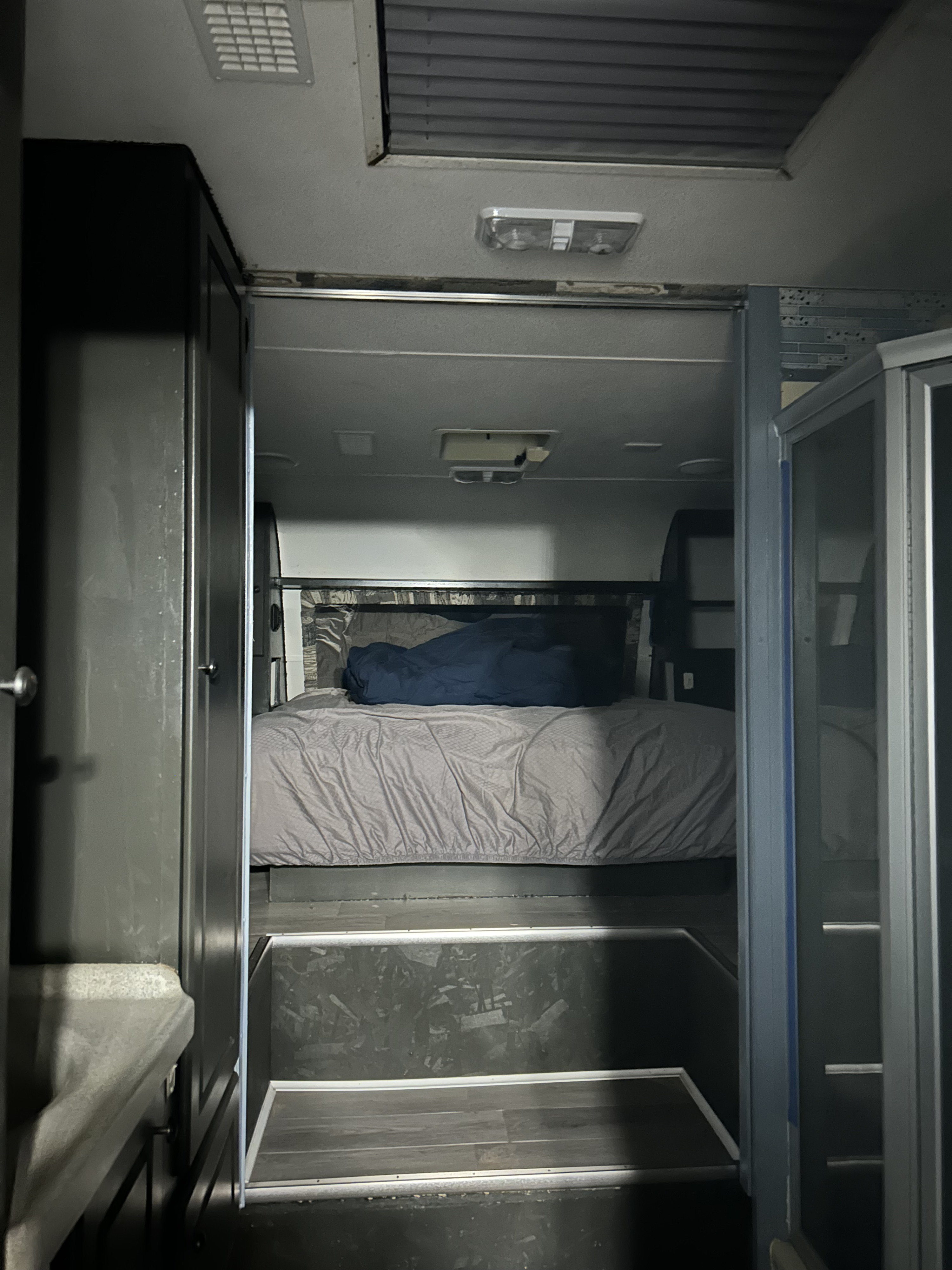 RV rental interior: dim view of a step-down bedroom with a made bed, dark walls, ceiling vents, and lighting fixtures.. Weekend Warrior 3705 2004