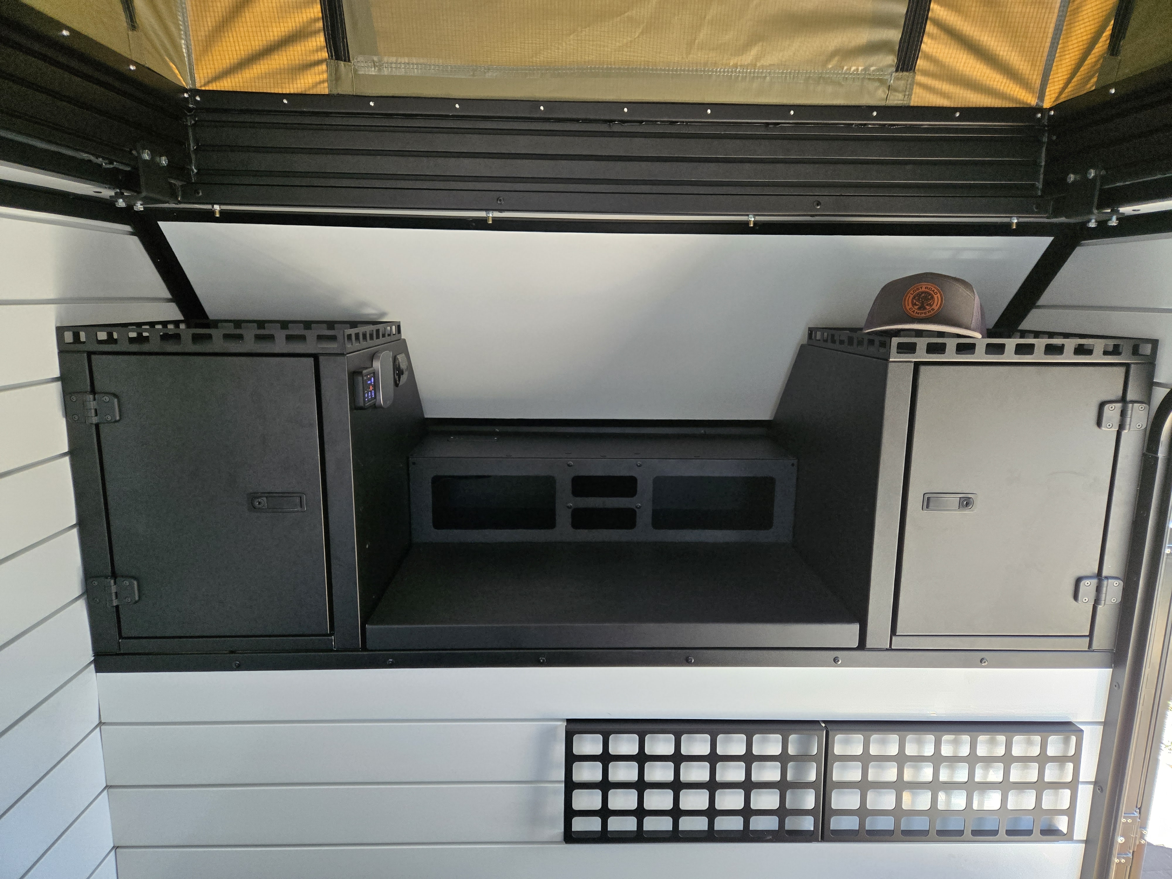 RV rental: Camper interior with dark storage cabinets, central platform, control panel, and a pop-top tent section above.. Lost Road Campers Luna pop top 2025