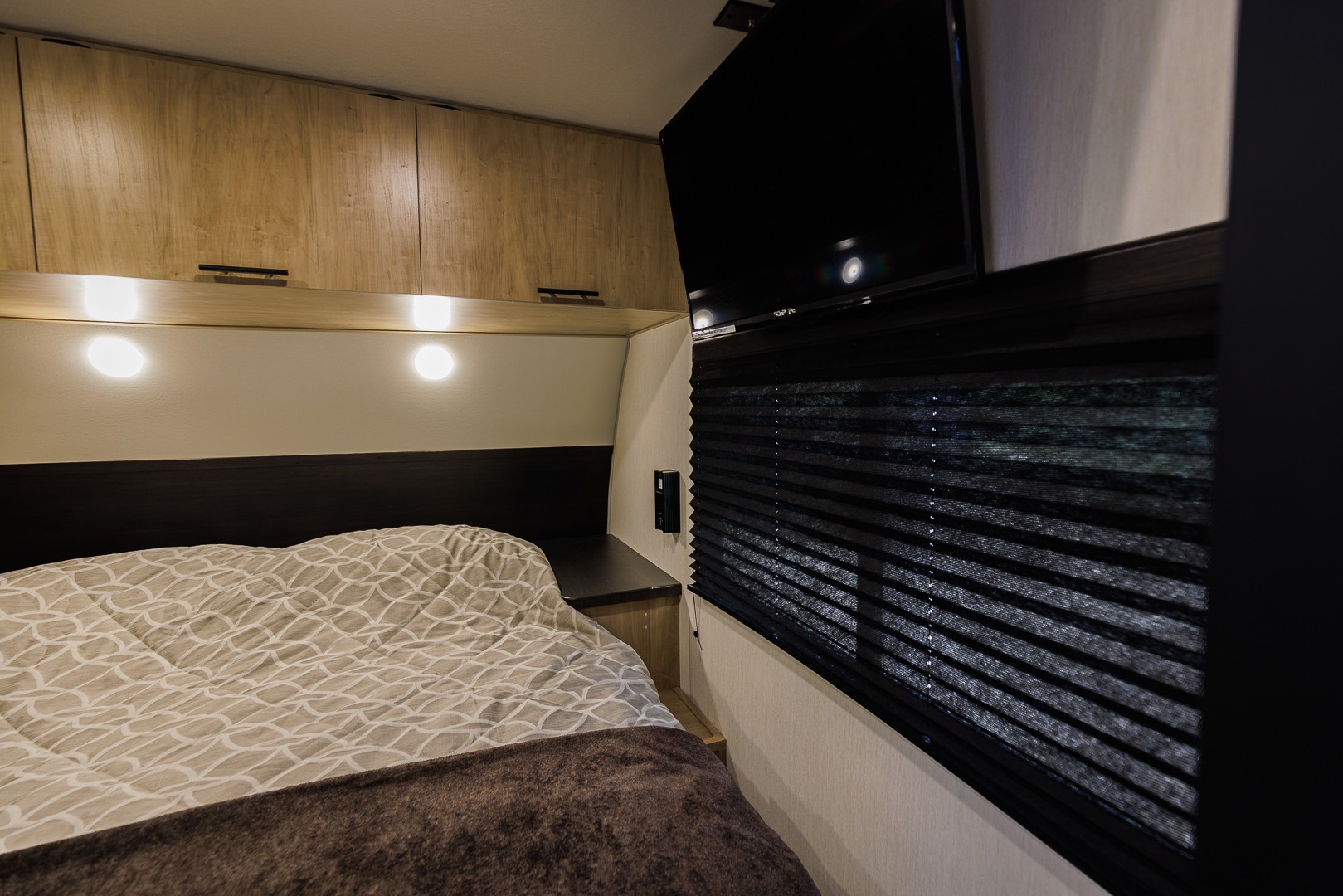 Cozy RV rental bedroom with a comfortable bed, overhead cabinets, TV, and pleated window blind.. Forest River Cherokee Grey Wolf 2026