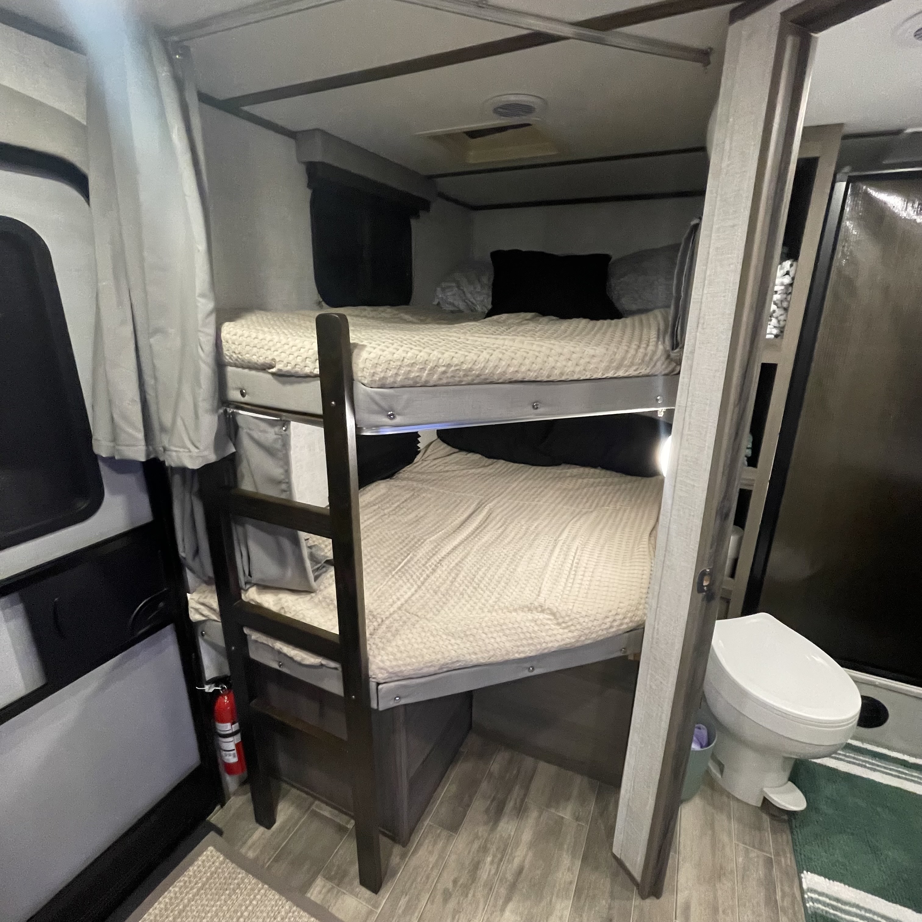 Cozy RV rental interior with bunk beds, a compact toilet, and a fire extinguisher, perfect for family travel.. Gulf Stream Envision 2023
