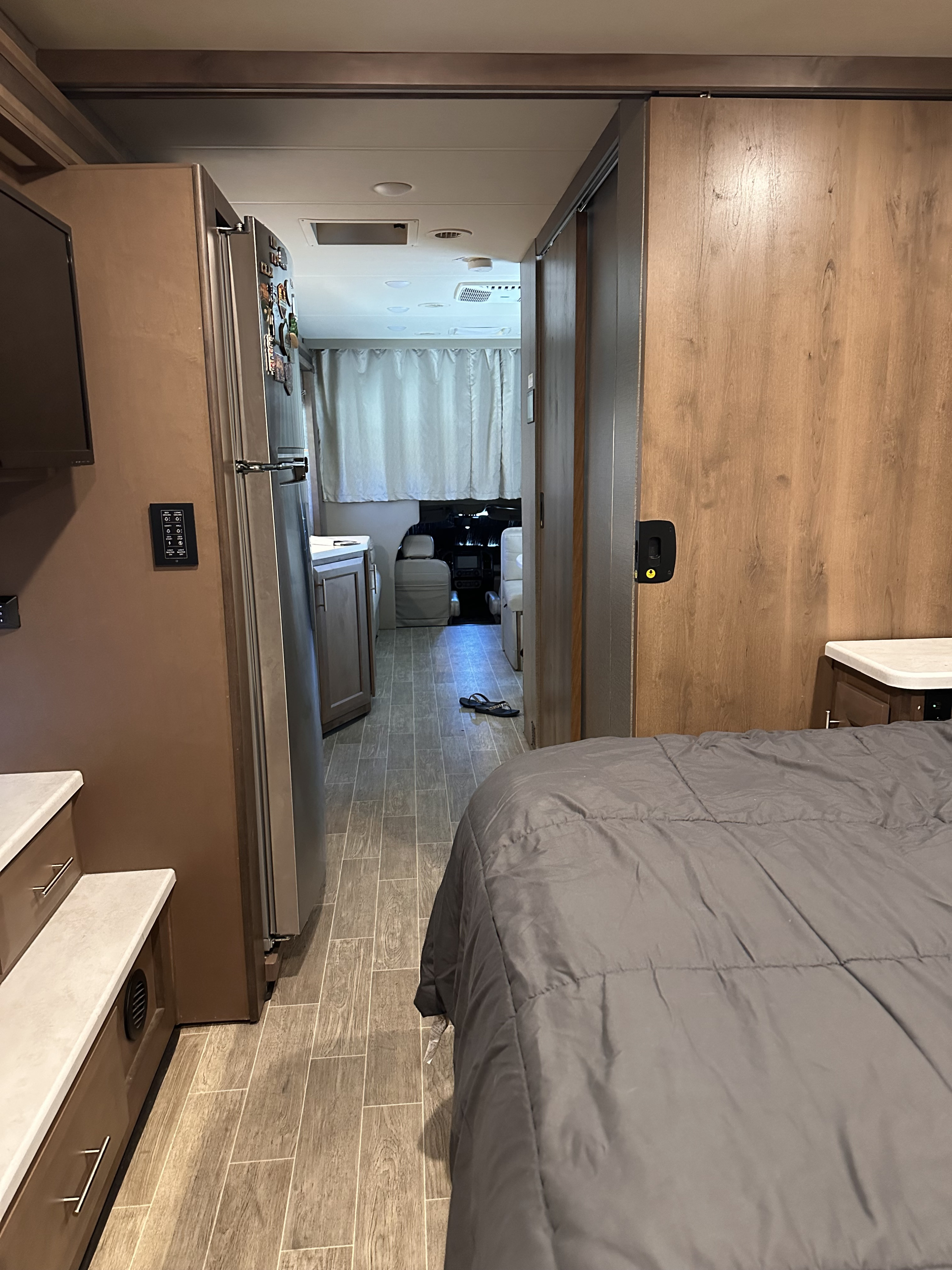 Inside an RV rental: hallway leading past kitchen and a partial view of the bedroom. Wood-look floor towards the cockpit.. Thor Omni 2021