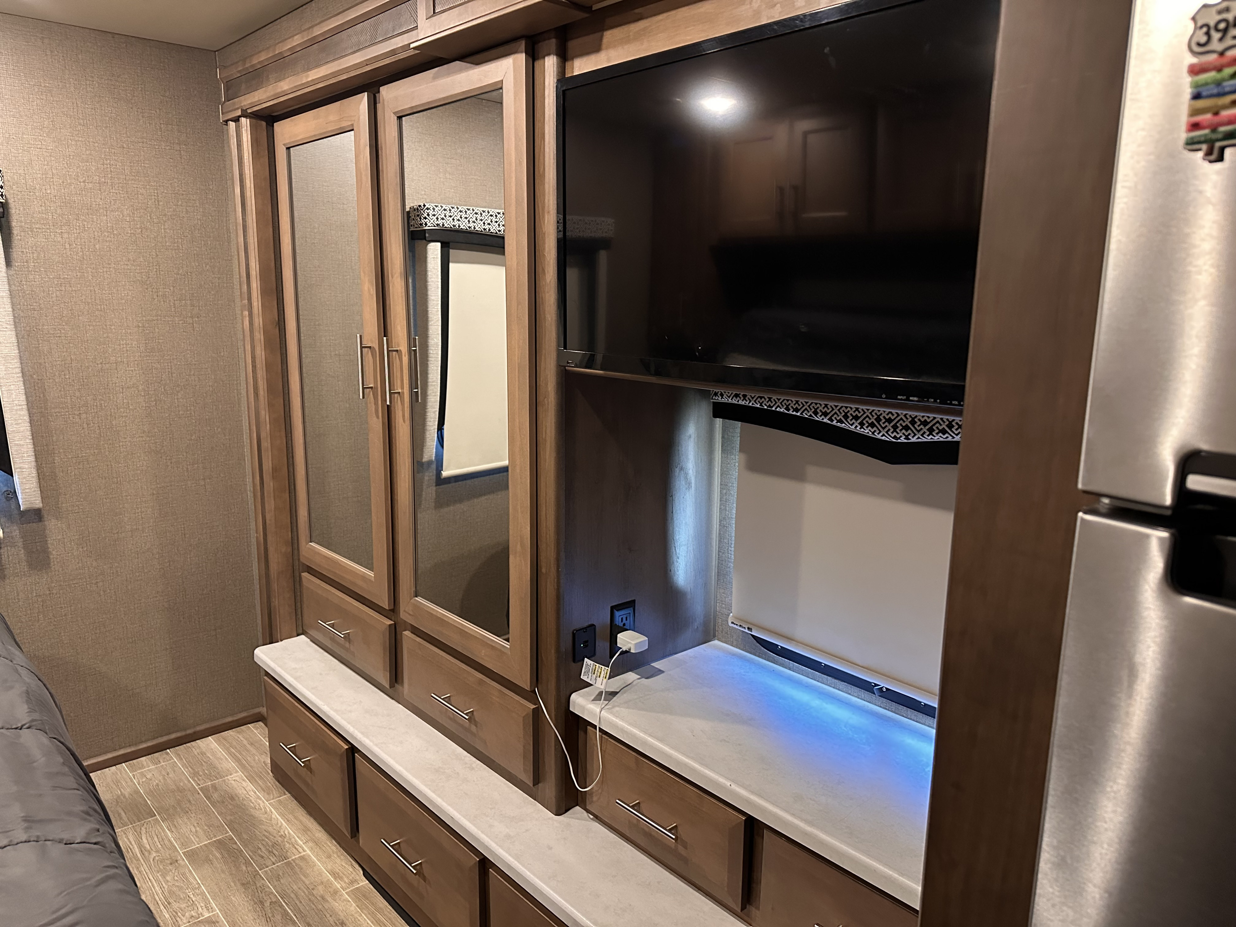 Modern RV rental bedroom with built-in TV, mirrored closet, drawers, and counter space for comfortable living.. Thor Omni 2021