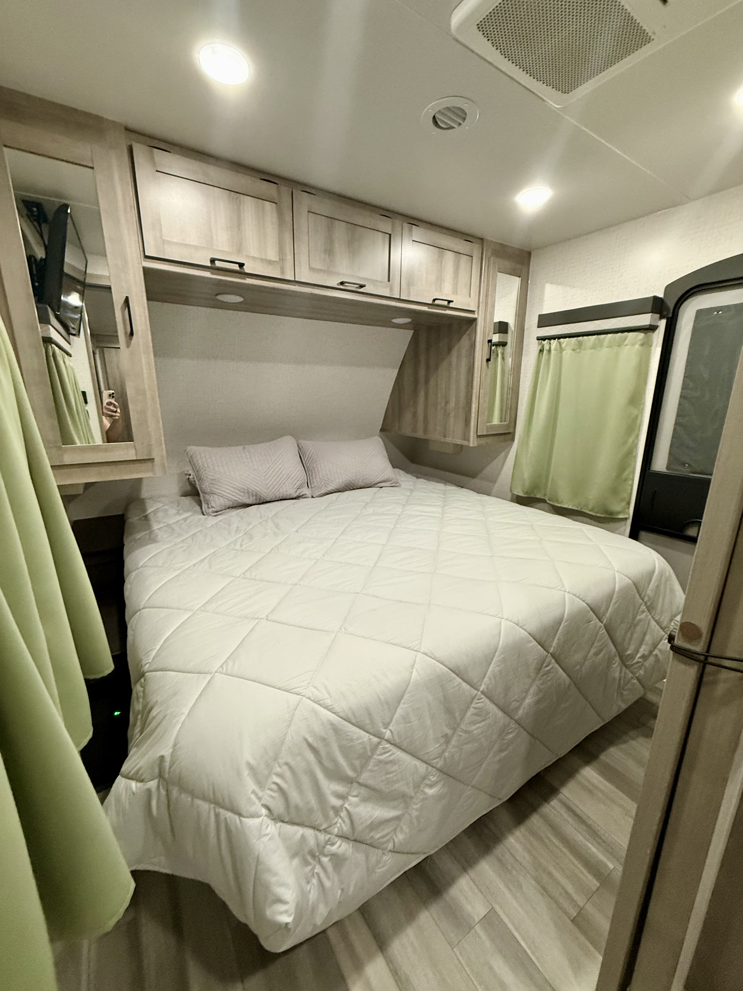 Cozy RV rental bedroom with a comfy bed, overhead cabinets, and light green curtains, perfect for a compact stay.. Winnebago Voyage 2022