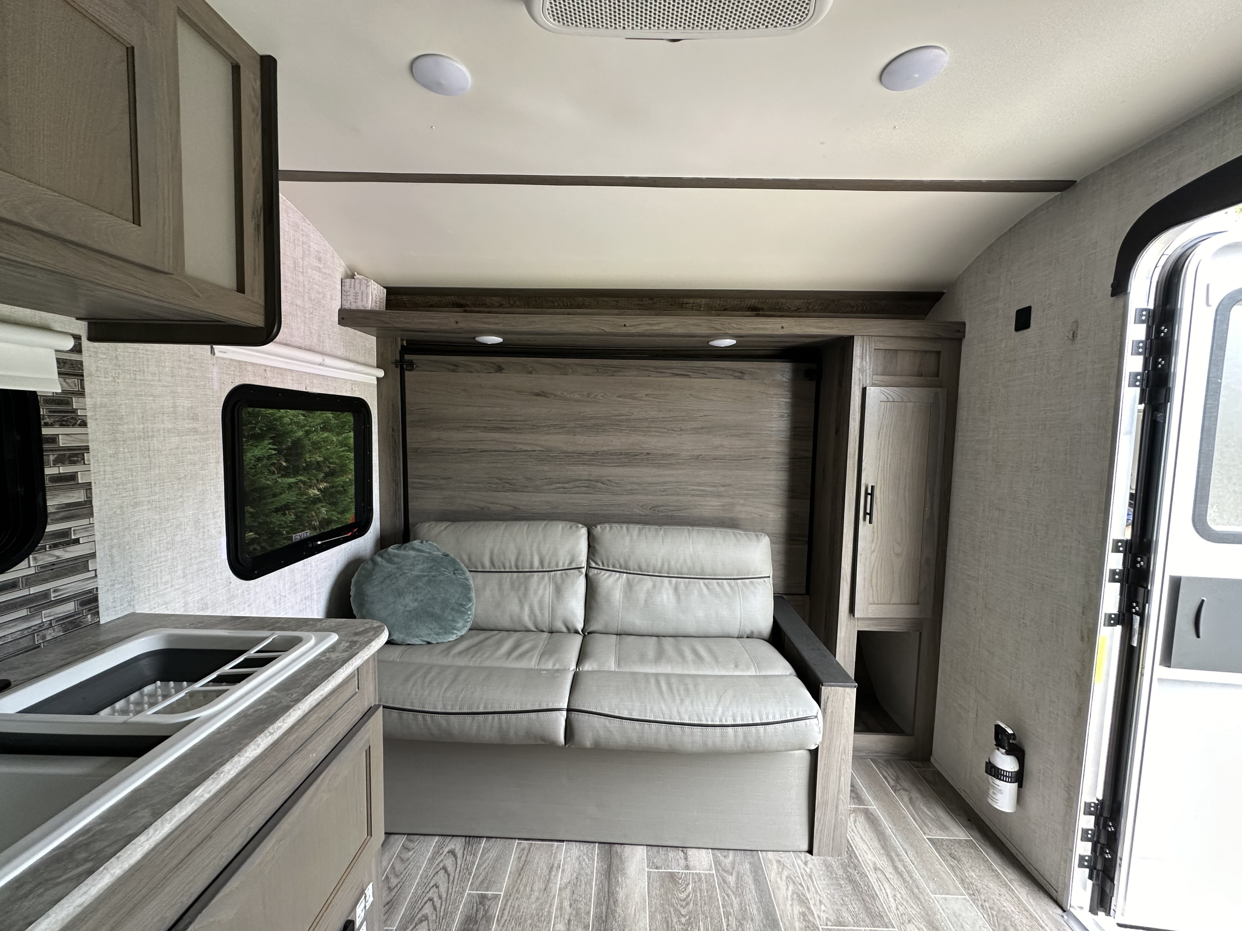 Modern rv rental interior featuring a gray sofa/wall bed, compact kitchen, wood-look floors, and neutral tones.. Gulf Stream Ameri-Lite 2021