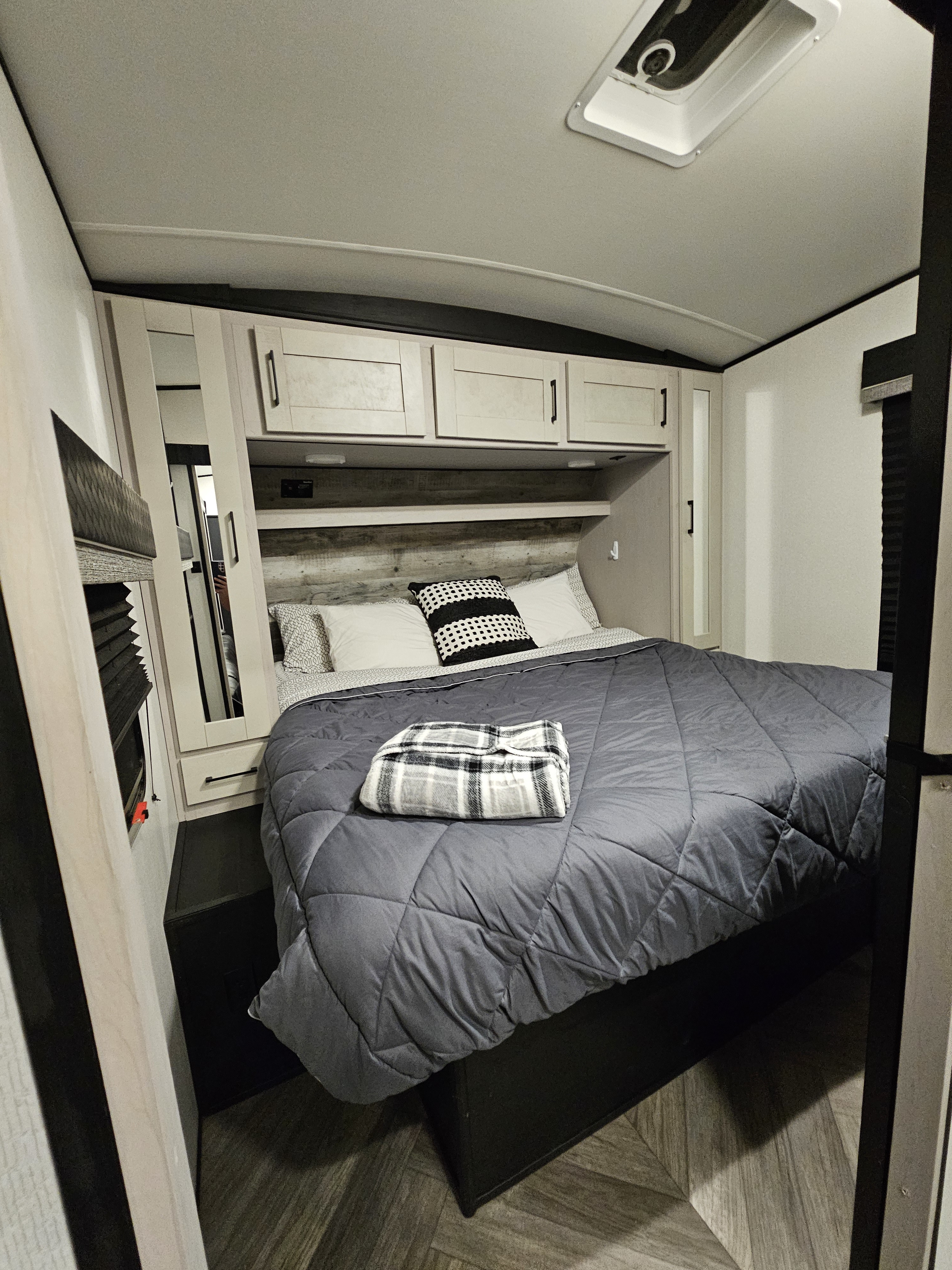Cozy RV rental bedroom featuring a gray bed with a plaid blanket, overhead cabinets, and mirrored storage.. Heartland RVs Torque Toy Hauler 2021