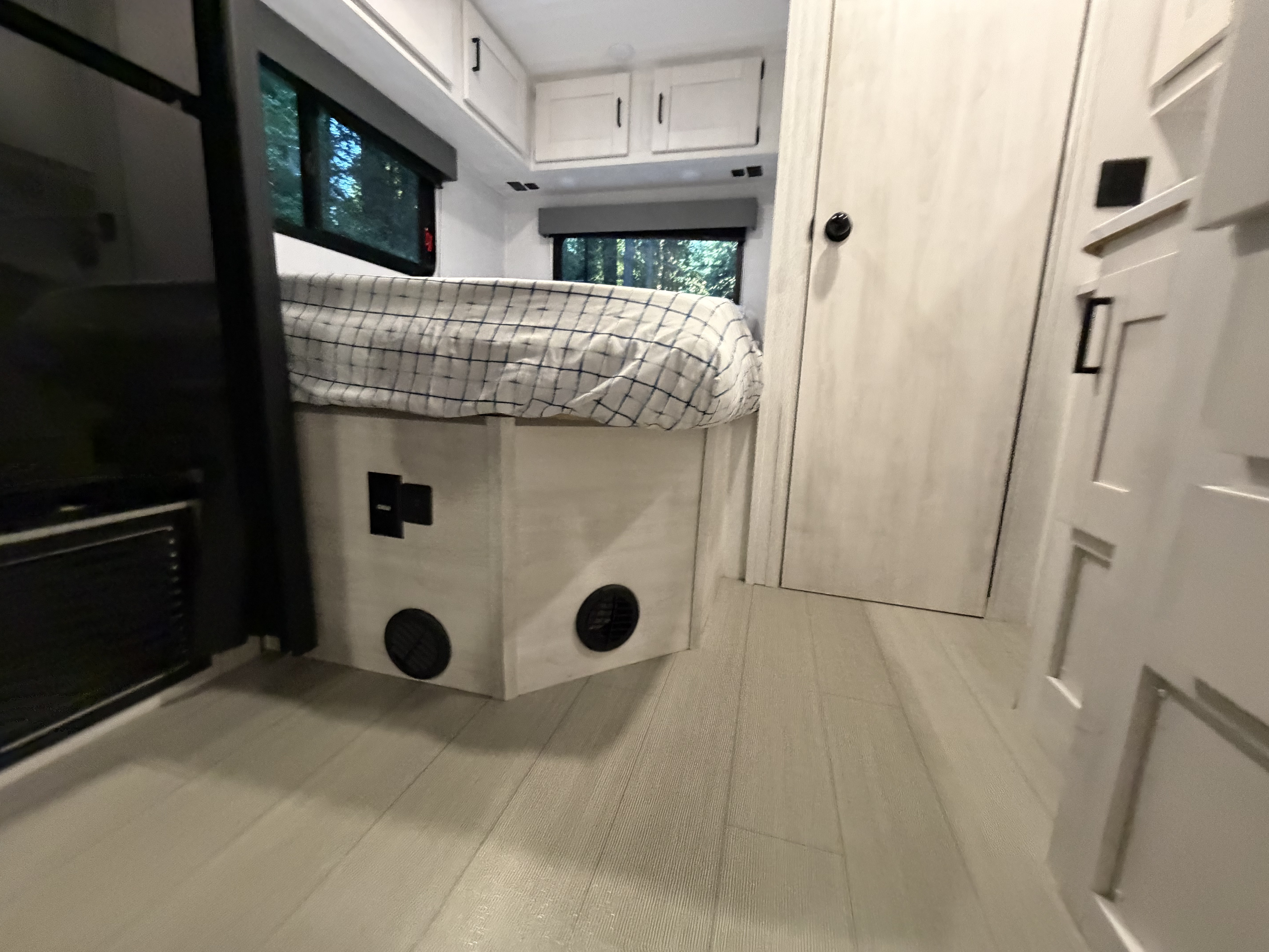 Modern RV rental bedroom: white cabinetry, comfy bed, windows to nature, and light wood flooring.. East to West Entrada 2025