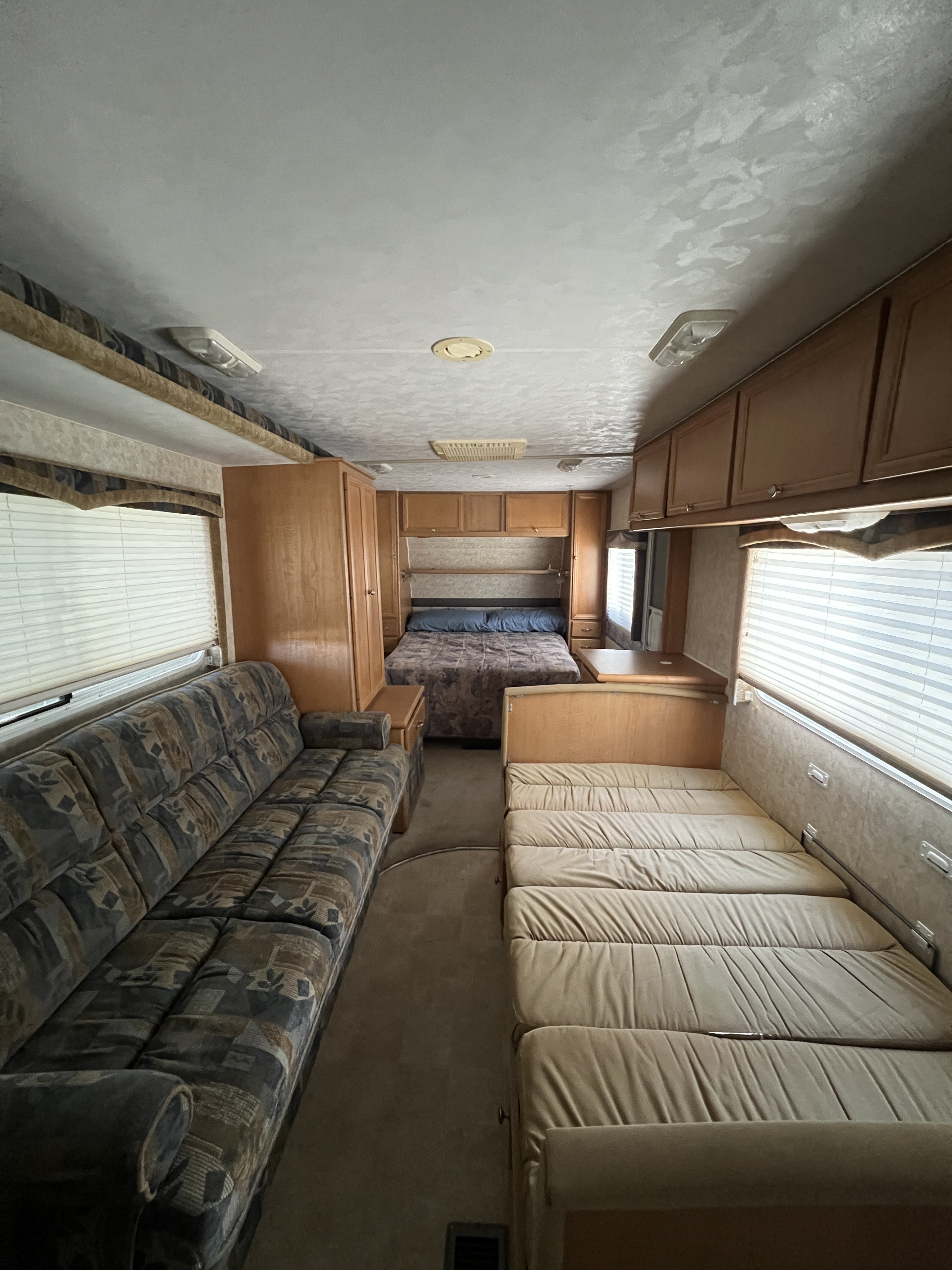Inside this RV rental: a patterned sofa, two beds, and wood cabinetry, offering a cozy living space for travel.. Alpenlite Aspen 2004