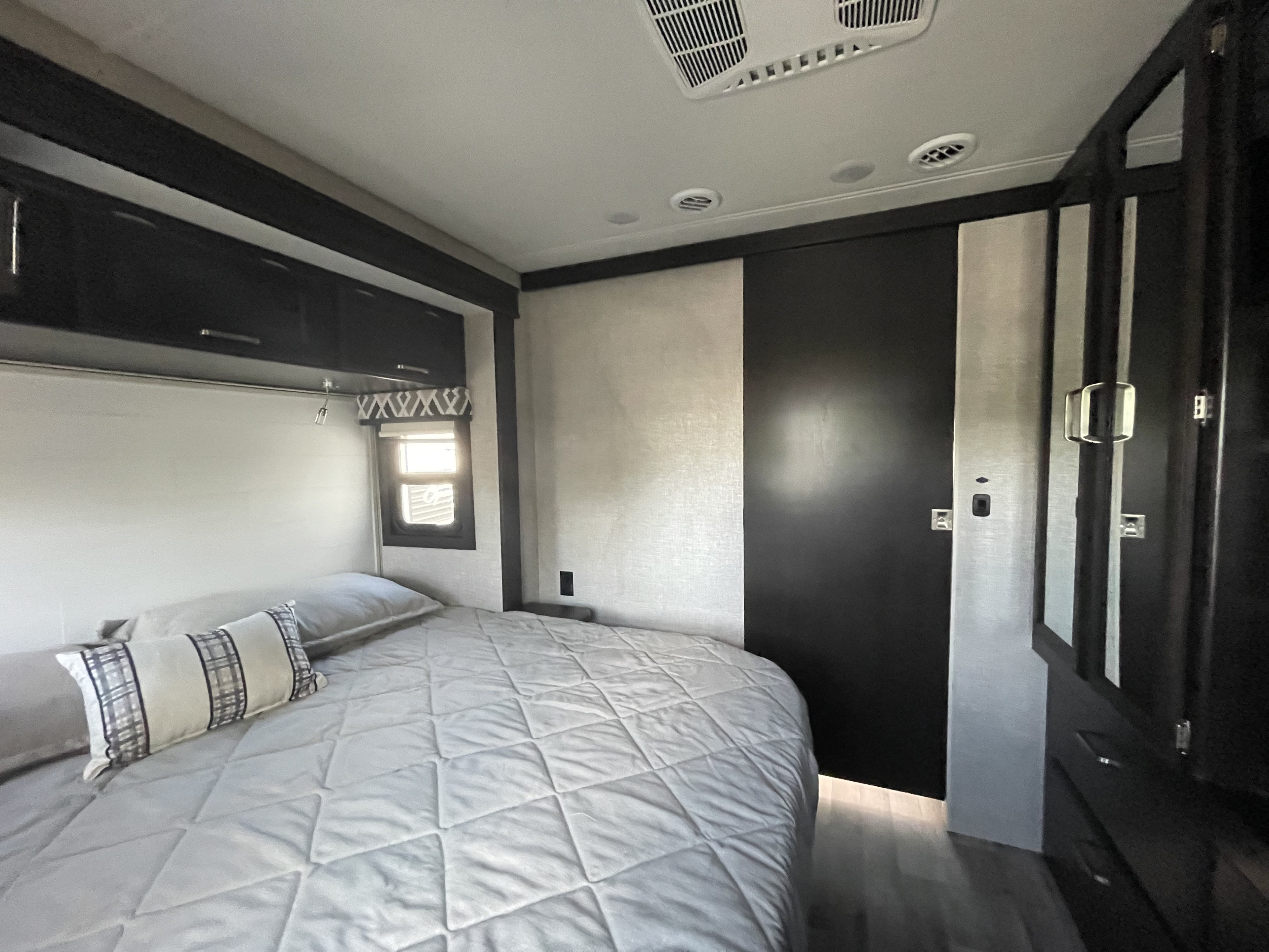 Interior of a comfortable RV rental bedroom with a quilted bed, overhead storage, and a dark sliding door.. Jayco Precept 2022