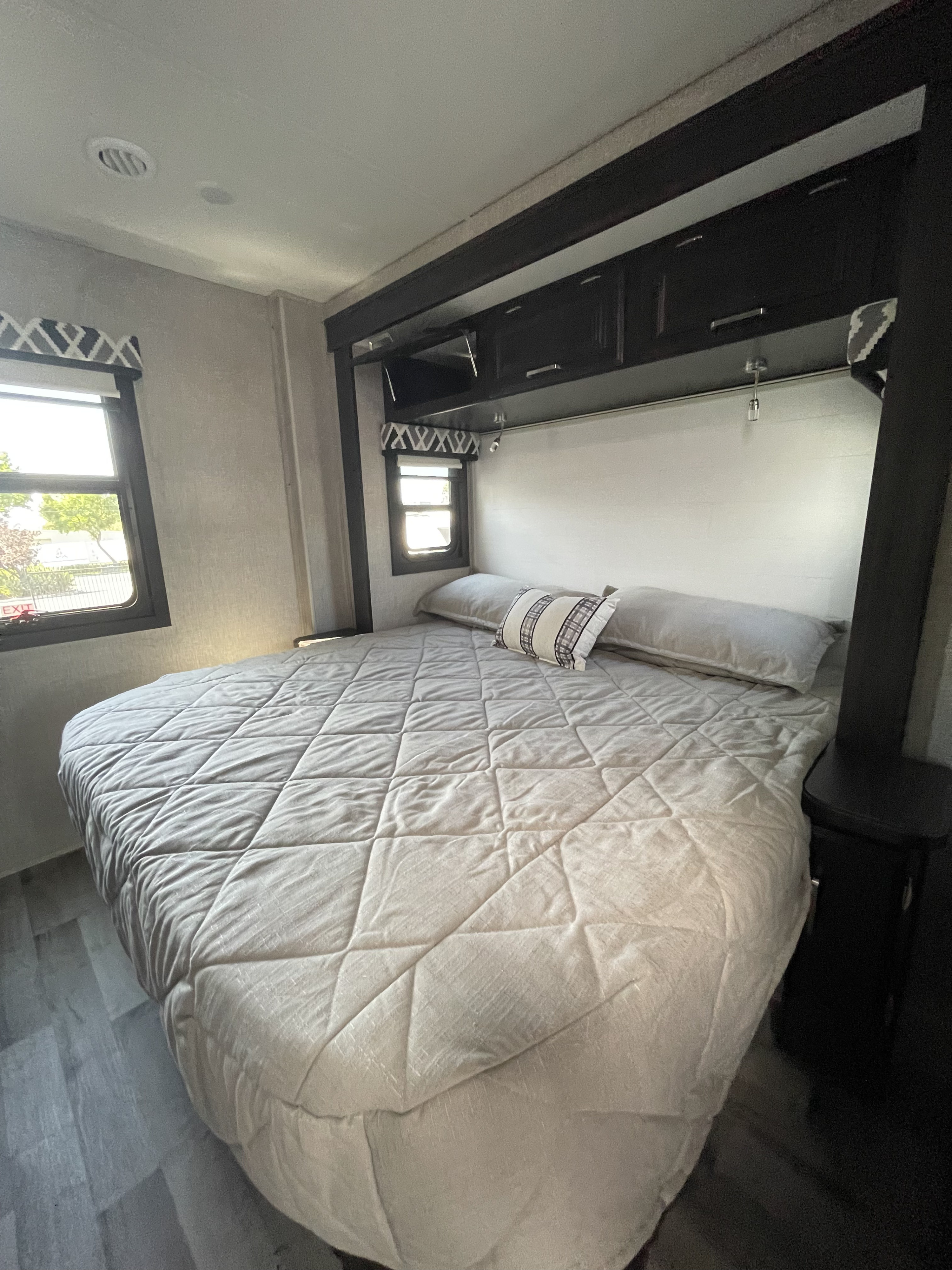Cozy rv rental bedroom with a large quilted bed, overhead storage, and windows, providing a comfortable interior.. Jayco Precept 2022