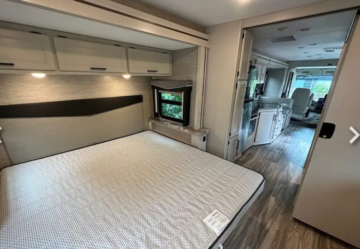 Spacious RV rental interior with a comfortable bedroom, overhead storage, and open living area. Perfect for travel!. Thor Resonate 2023