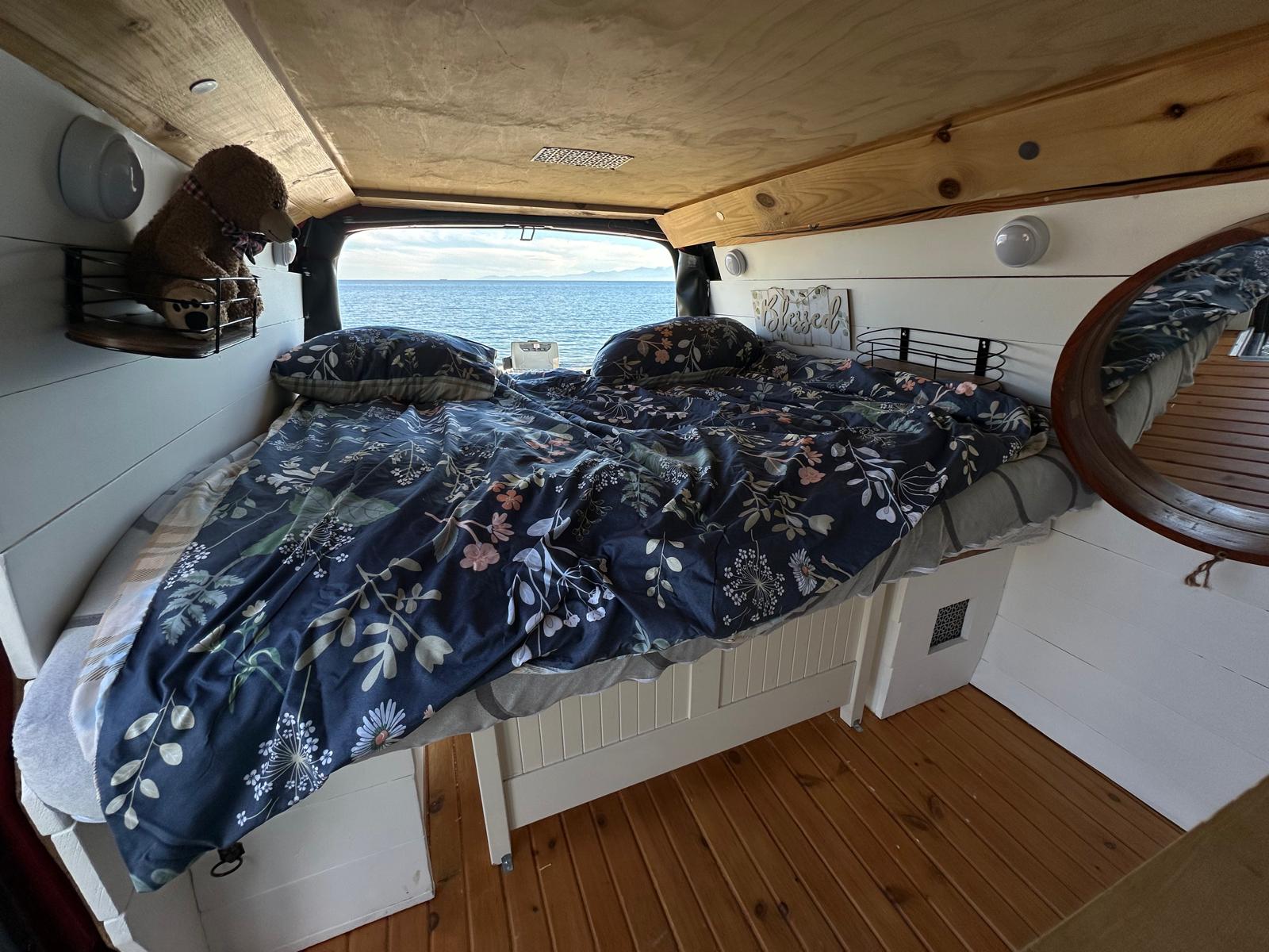 Experience van life in this cozy RV rental bedroom. Wake up to ocean views from your comfortable floral bed.. Gmc Savanna 2003
