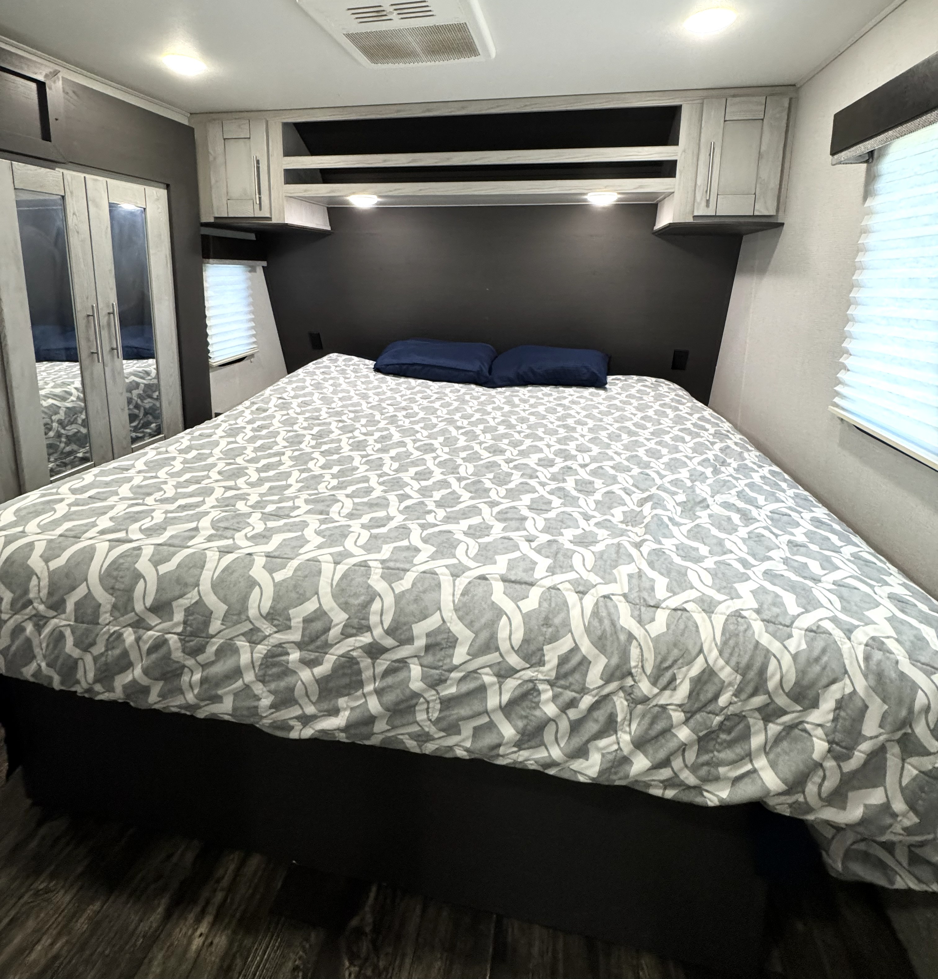 Cozy RV rental bedroom featuring a queen bed with a patterned comforter, overhead storage, and a mirrored closet.. Keystone Fuzion 2021
