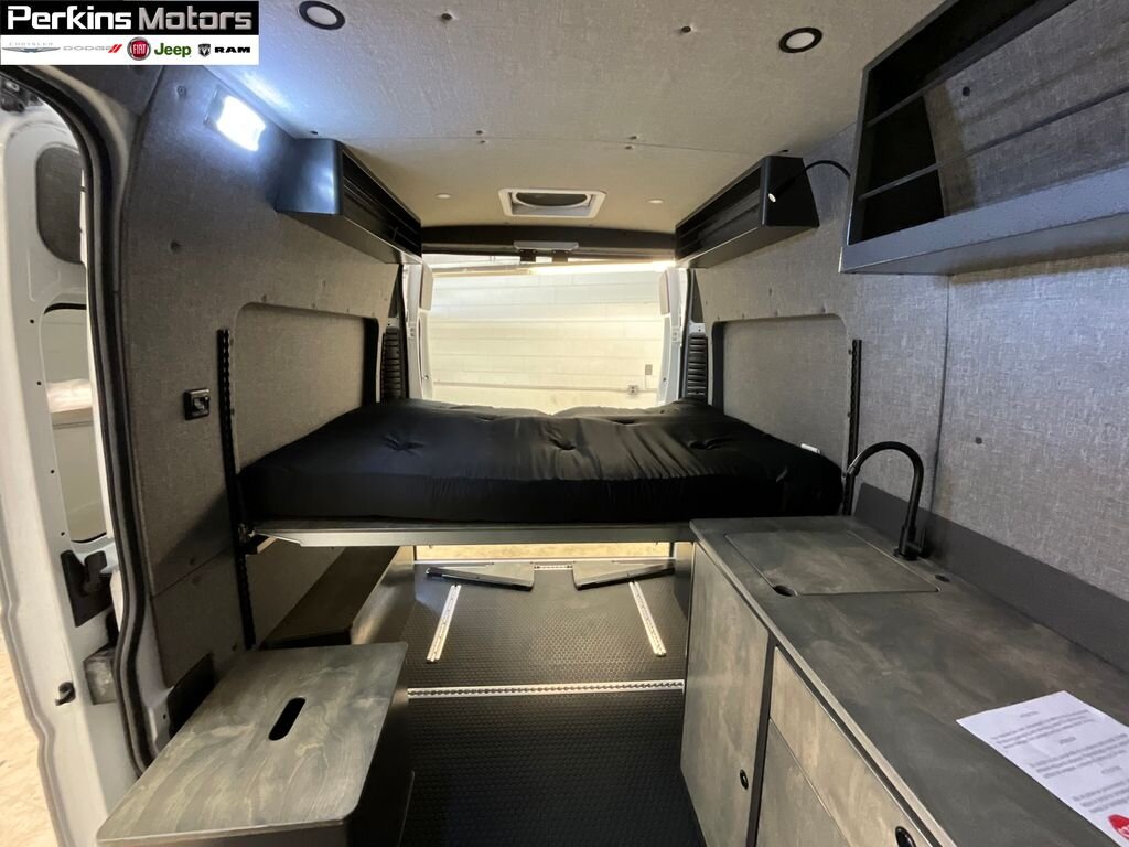 RV rental interior featuring a raised bed with black mattress, kitchenette with sink, and sleek gray finishes.. Ram Promaster 1500 2024