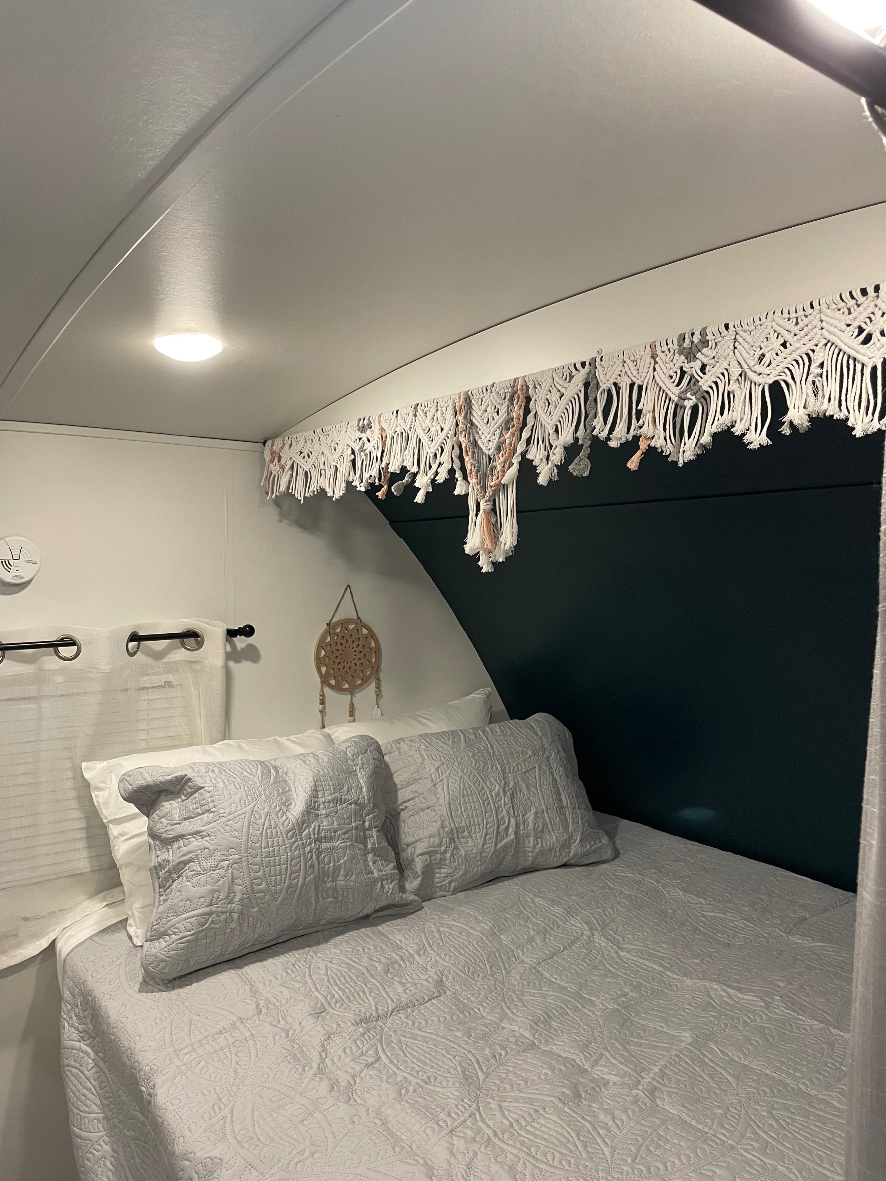 Cozy RV rental bedroom featuring soft, quilted bedding, a dark accent wall, and a unique macrame valance above the bed.. Keystone RV Passport Grand Touring 2020
