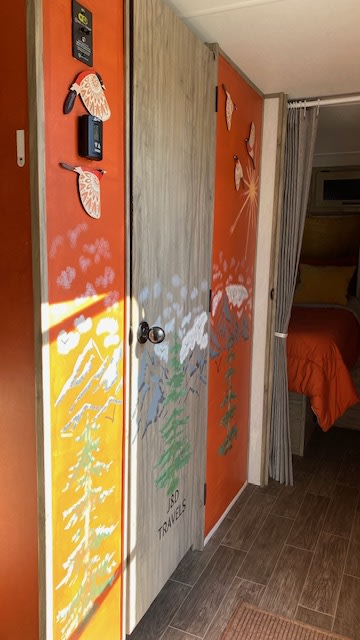 Explore a vibrant RV rental interior featuring custom-painted nature-themed doors and a peek into the cozy bedroom area.. Forest River Cherokee Alpha Wolf 2021