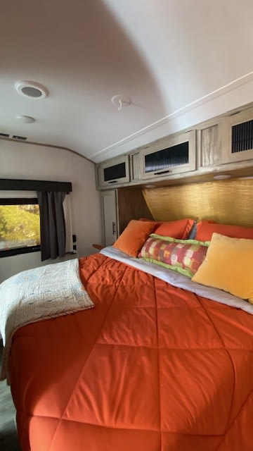 Comfortable RV rental bedroom featuring bright orange bedding, colorful pillows, and overhead cabinets.. Forest River Cherokee Alpha Wolf 2021