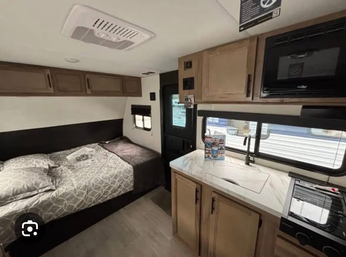 Modern RV rental interior: a compact kitchen with sink/stove, and a cozy bed with overhead cabinets, ideal for travel.. Forest River Cherokee Wolf Pup 2024