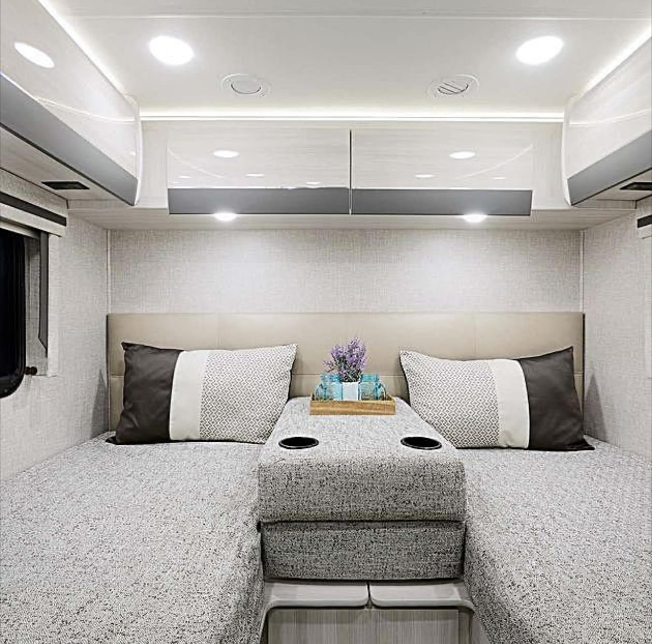 Stylish RV rental bedroom: twin beds, central console, and sleek overhead storage in a bright, neutral-toned interior.. Thor Compass 2024