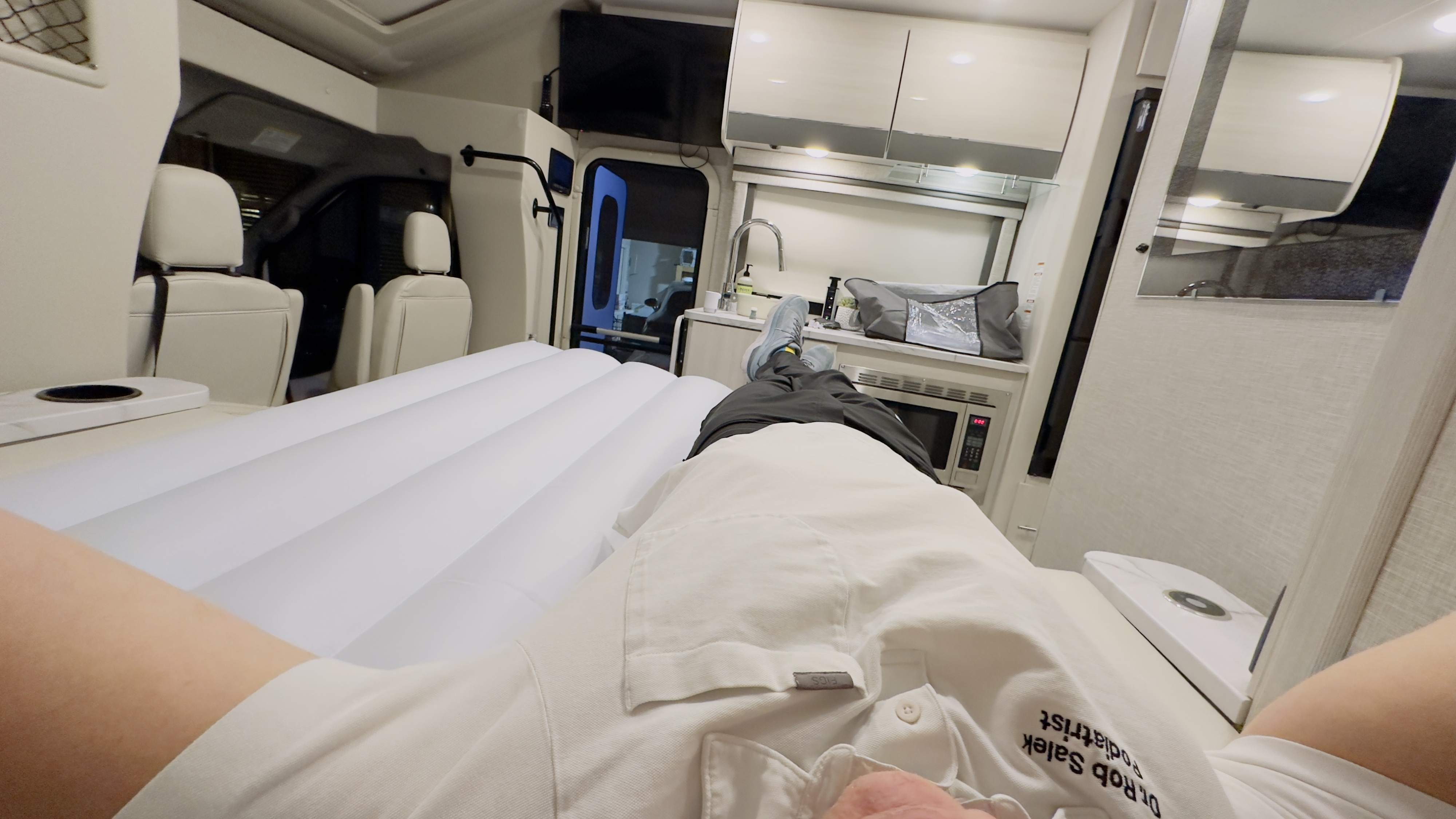First-person view inside a modern rv rental. Relaxing on an inflatable bed, with a compact kitchen, cabin seats, and TV visible for travel.. Thor Compass 2024