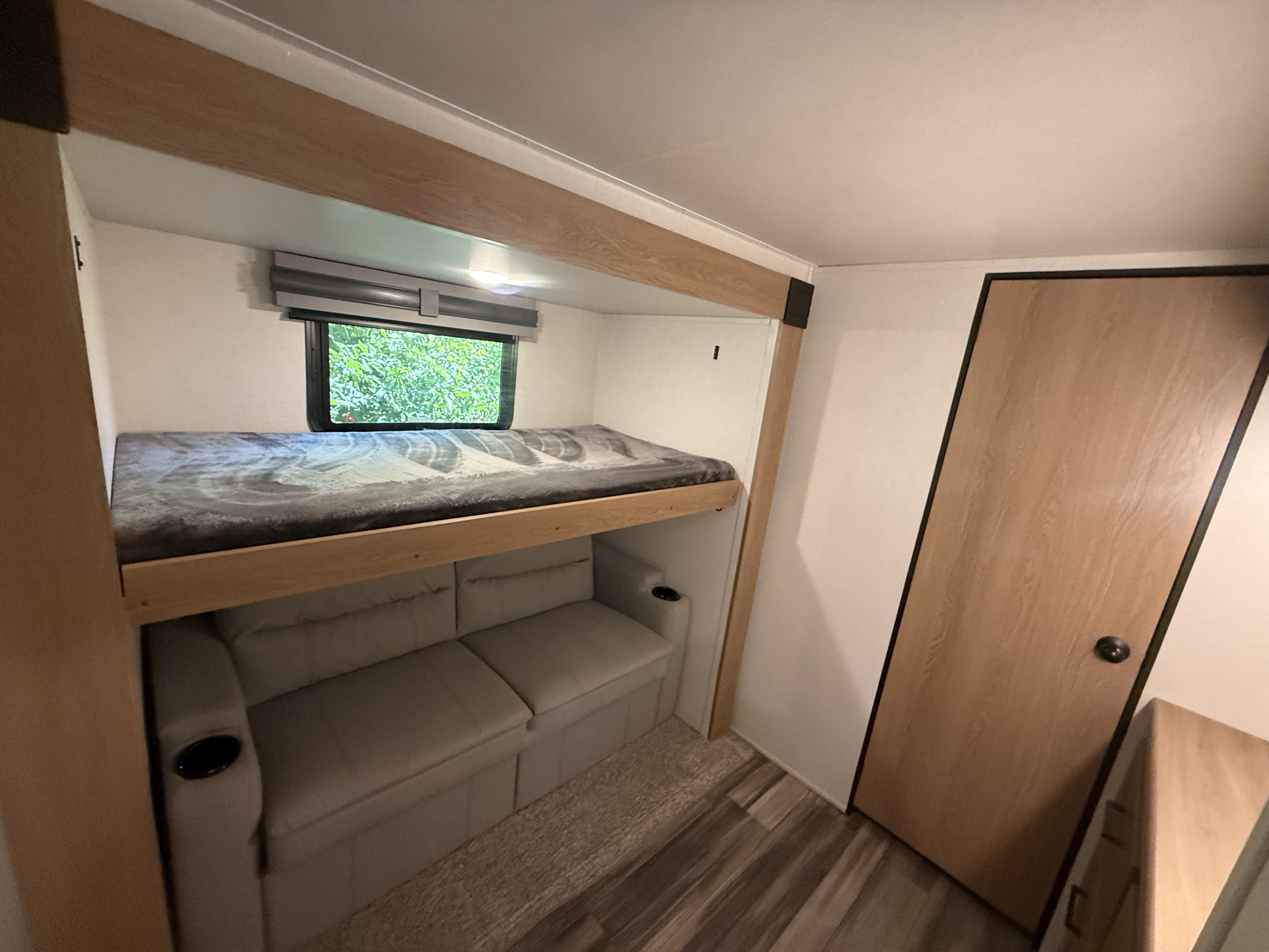 Inside an RV rental: a cozy bunk bed above a two-seater sofa with a cup holder, next to a window with green views.. Other Sanibel 3902WB 2022