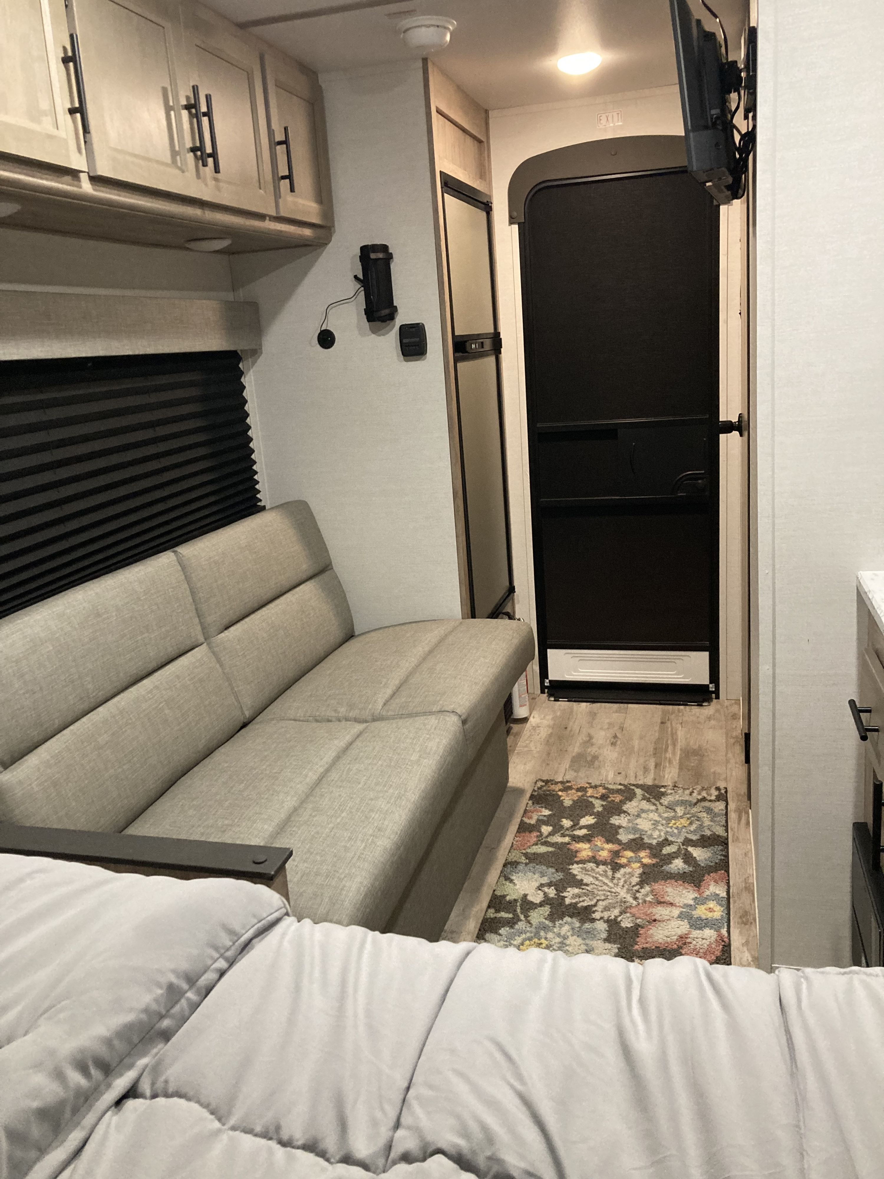 RV rental interior: light wood cabinets, grey sofa, window with blinds, TV, and door in a travel trailer living space.. Gulf Stream Yellowstone Trail Edition 150RD 2025