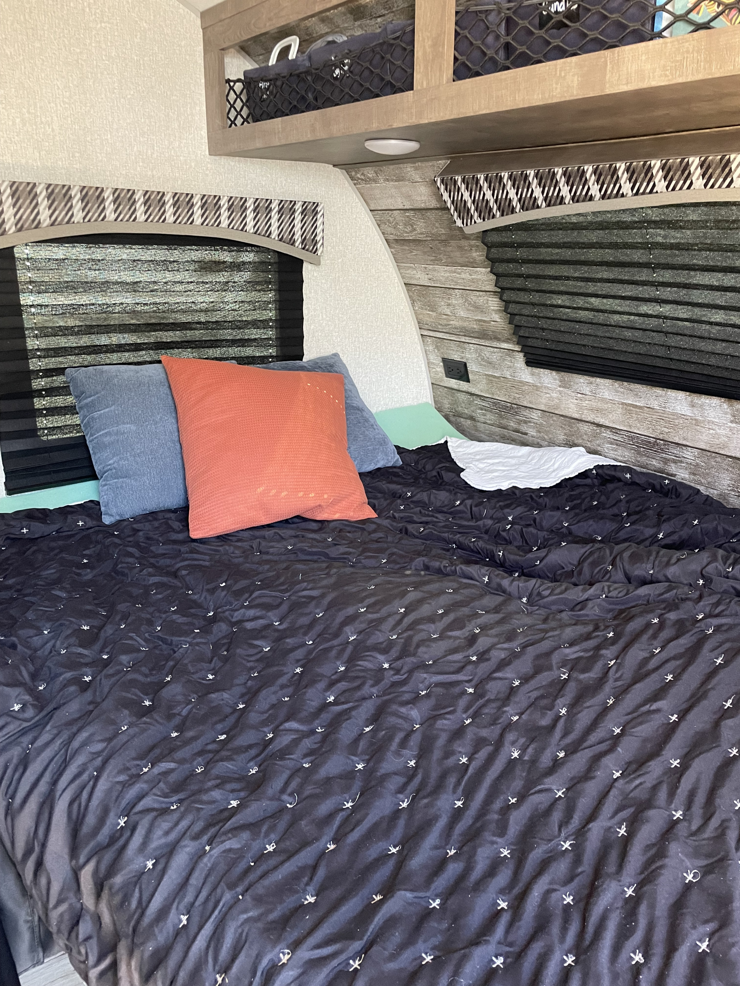 Inside an RV rental: a cozy bedroom featuring a dark quilted comforter, colorful pillows, and patterned window blinds.. Venture Sonic Lite VBH 169 2022