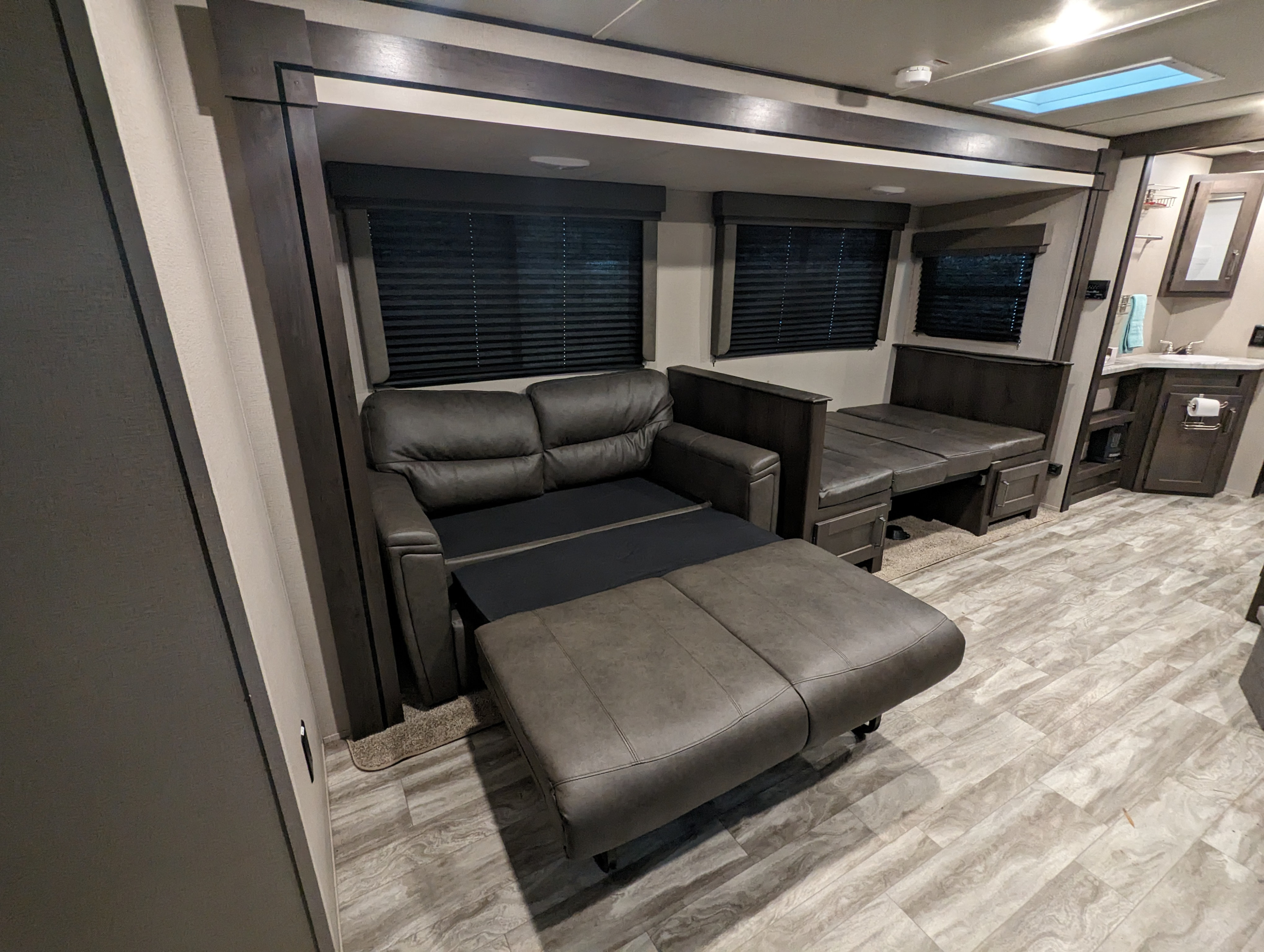 Modern rv rental living area with an extended sofa bed, dinette seating, dark wood trim, and light wood-style flooring.. Grand Design Transcend Xplor 2022