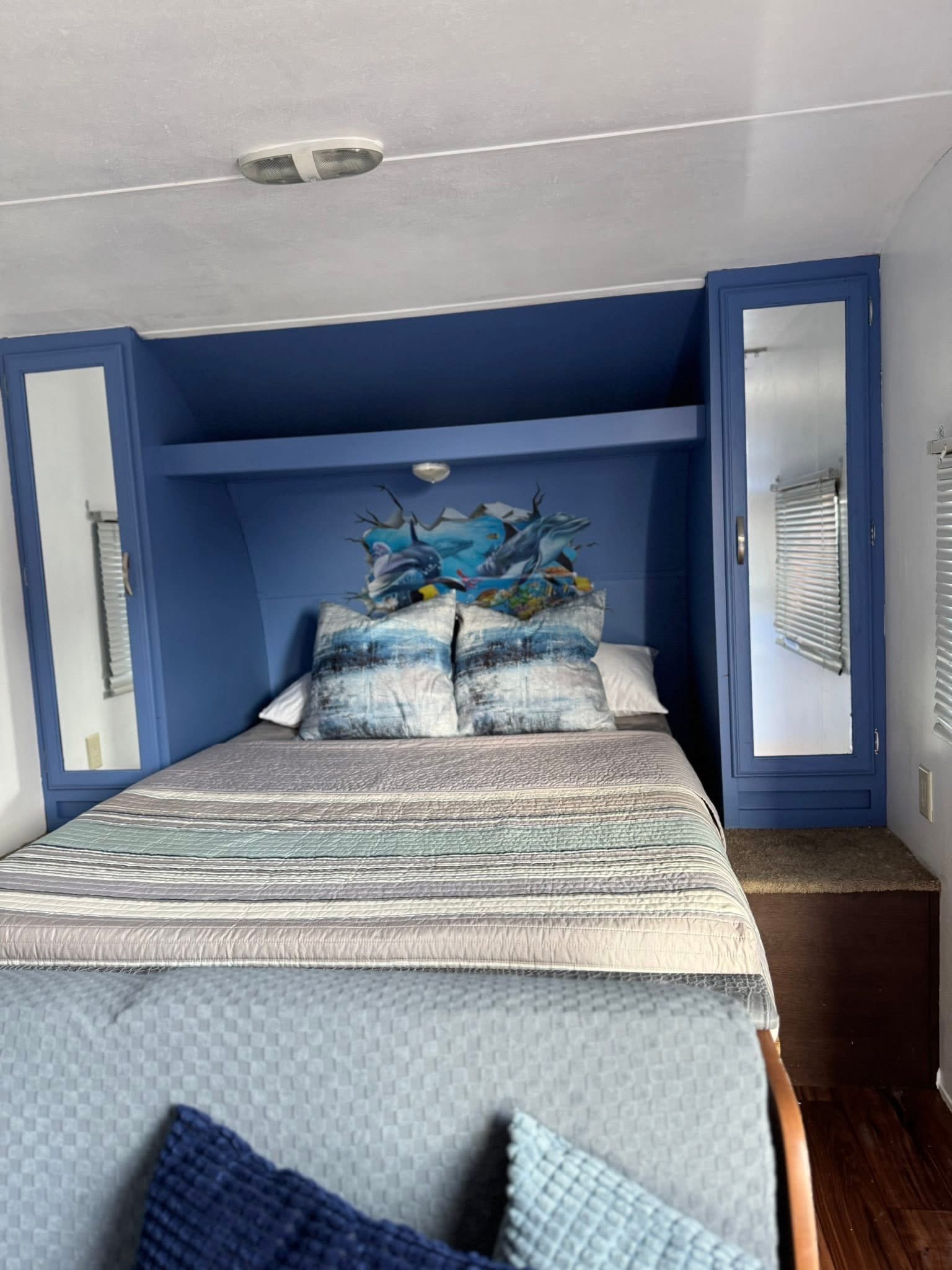 Cozy RV rental bedroom featuring a bed with striped bedding, blue headboard with a dolphin mural, and mirrored cabinets.. Forest River Wildwood X-Lite 2016