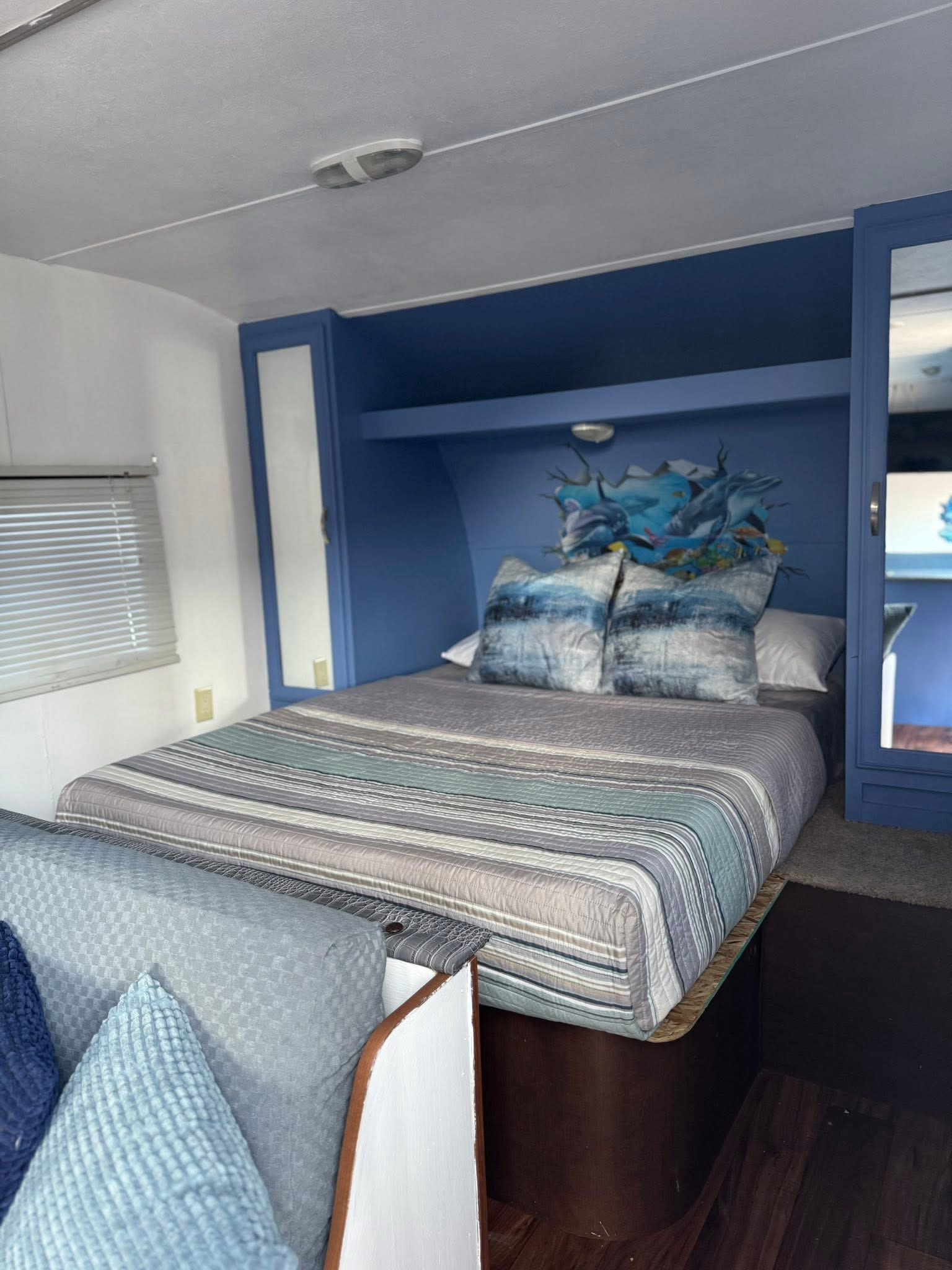 Inside this cozy rv rental bedroom, a bed with striped covers sits against blue cabinetry, featuring a vibrant dolphin mural.. Forest River Wildwood X-Lite 2016