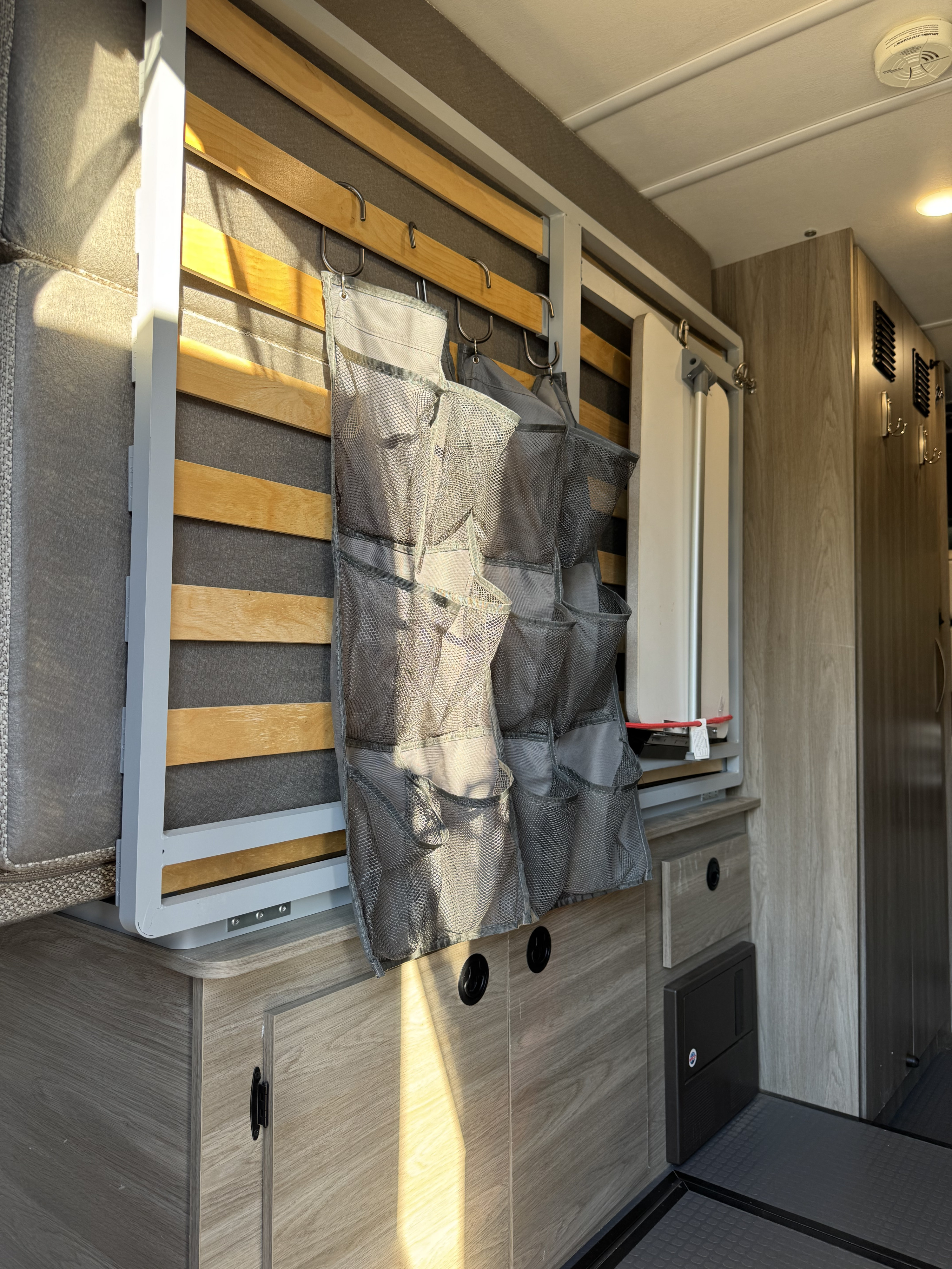 Inside this RV rental: folded bed with mesh storage, cabinets, and a compact table. Ideal for maximizing space on the go.. Winnebago Solis PX 2021