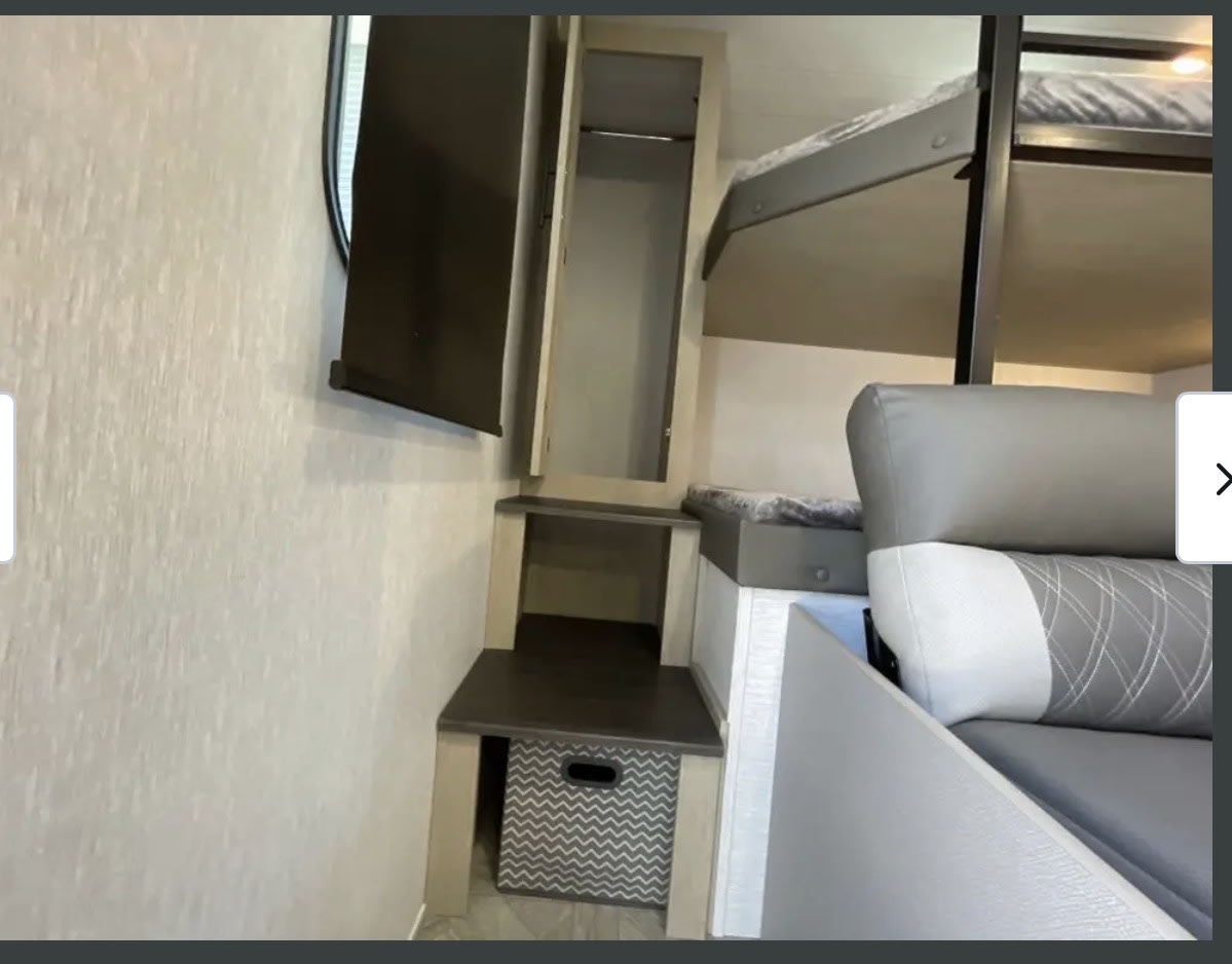 This RV rental interior reveals bunk beds, a grey sofa, wall-mounted TV, and built-in storage with a chevron bin.. Forest River Wildwood 2024