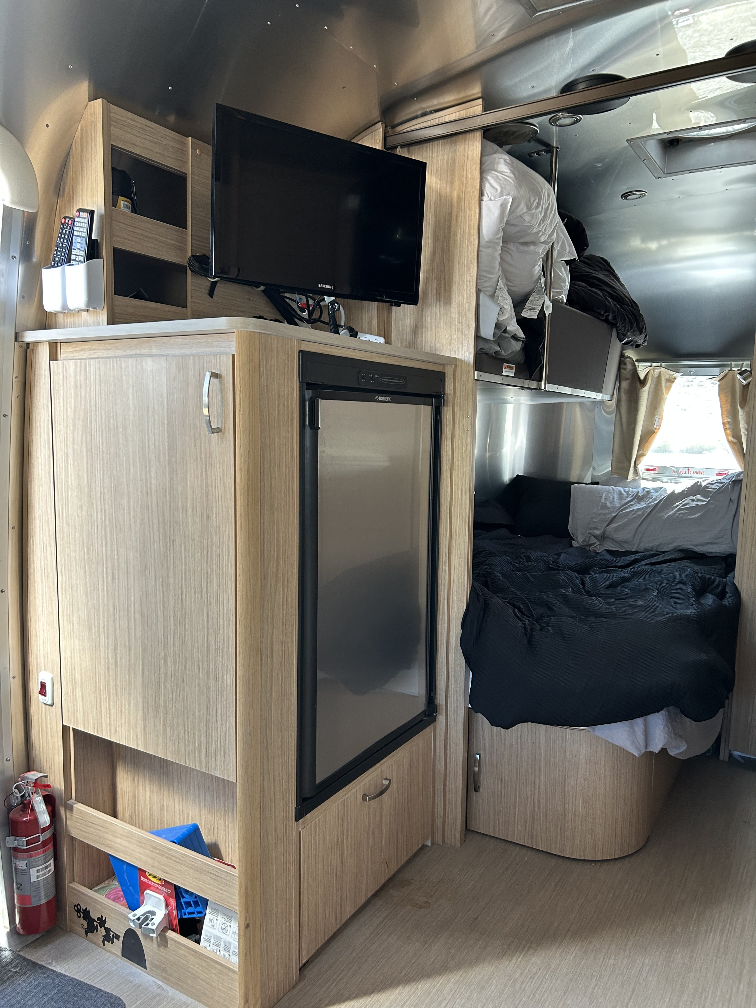 Modern rv rental interior showcasing sleek cabinetry, a wall-mounted TV, Dometic fridge, and a comfortable bed area.. Airstream Flying Cloud 2018