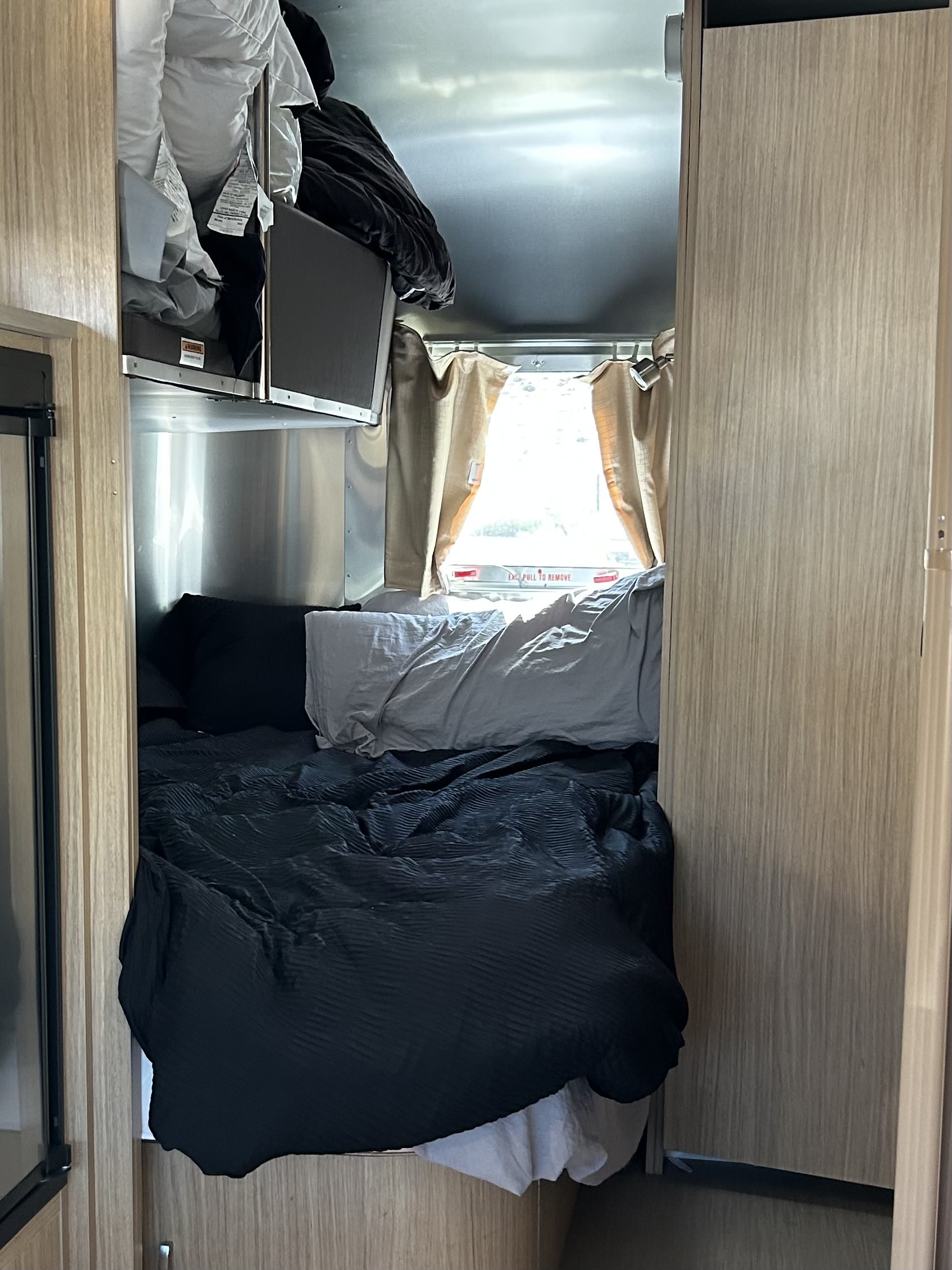 Cozy RV rental bedroom with dark bedding, overhead storage, and a bright window, showcasing a compact travel space.. Airstream Flying Cloud 2018
