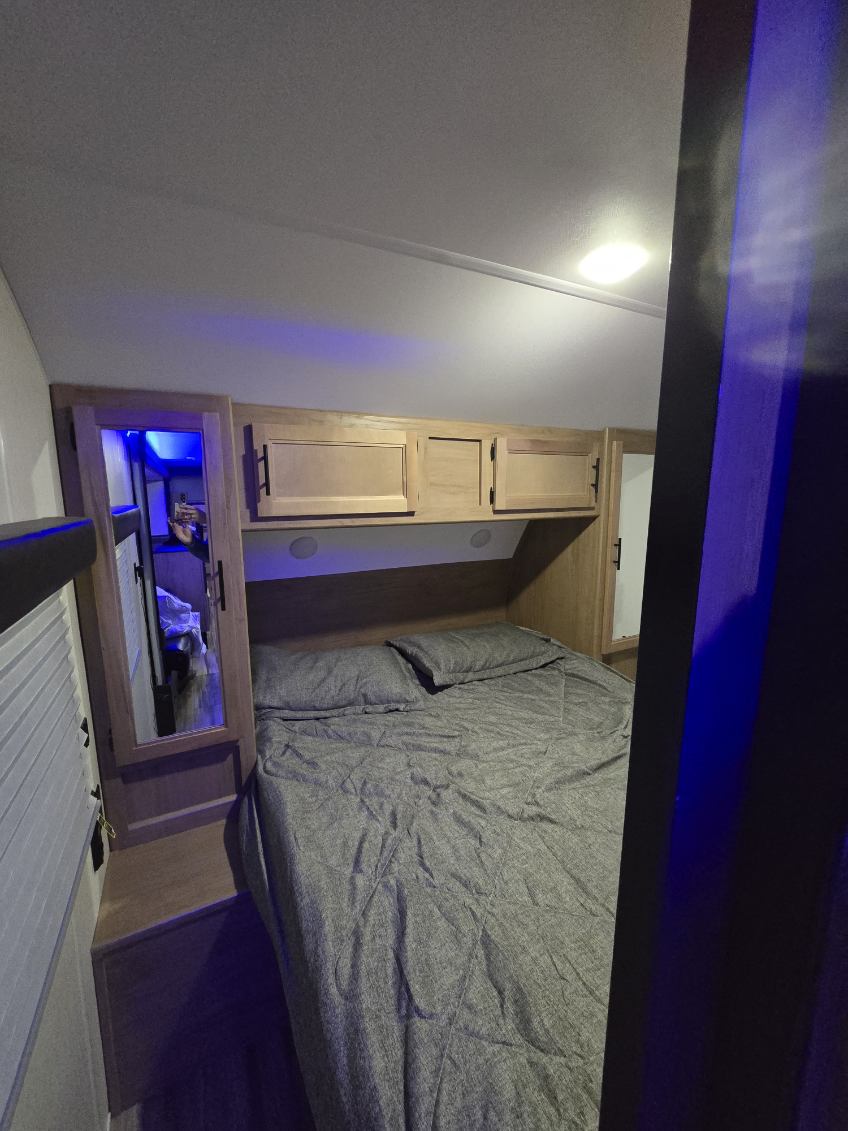 Cozy RV rental bedroom featuring a bed with gray bedding, overhead cabinets, and blue ambient lighting.. Forest River Cherokee Grey Wolf 2022