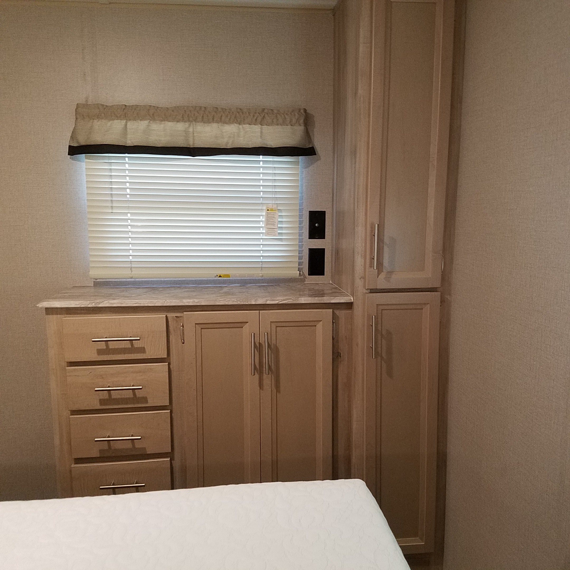 RV rental interior featuring a bedroom area with a window, blinds, countertop, drawers, and tall storage cabinets.. Coachmen Catalina 2021