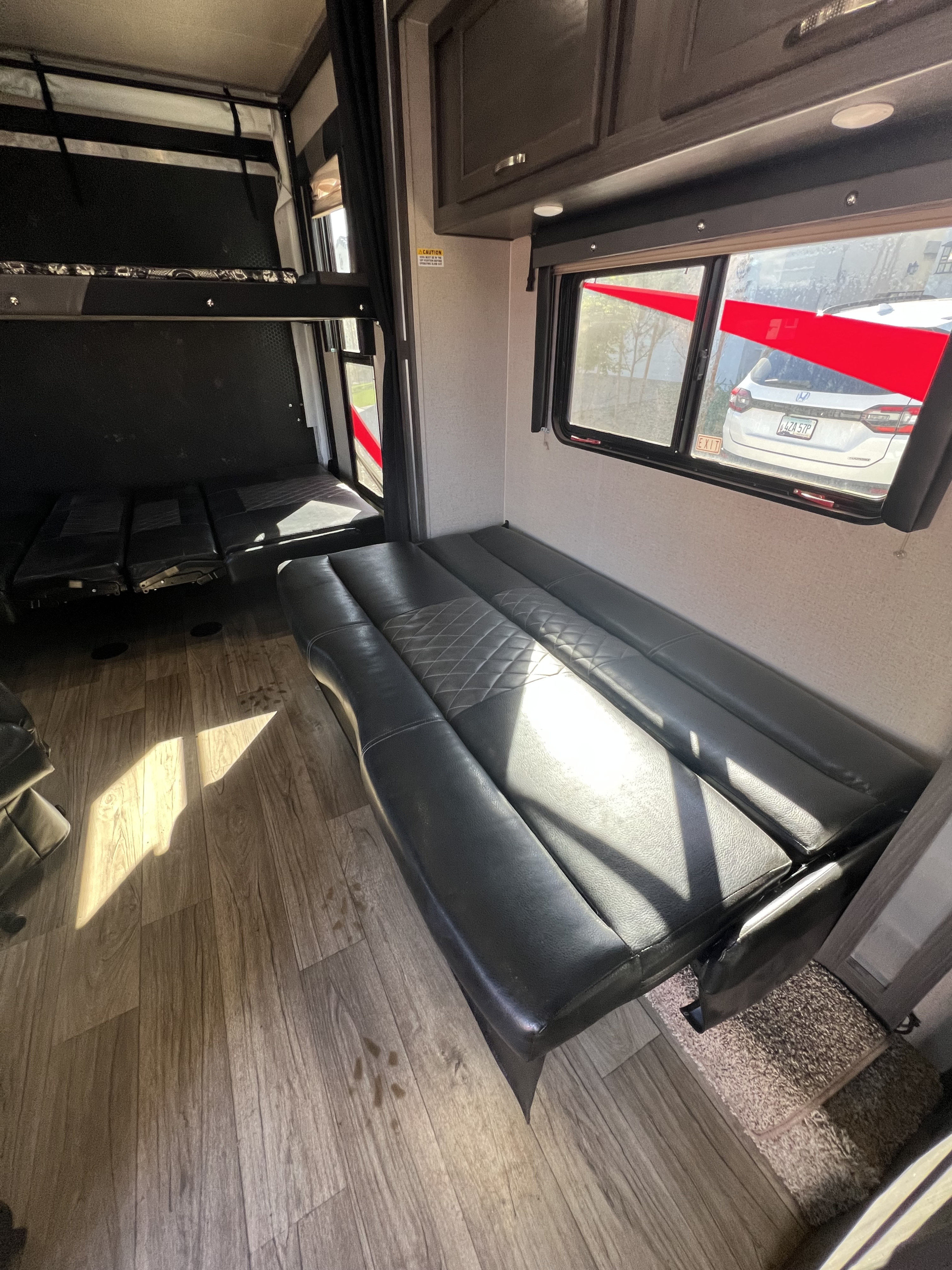 Inside an rv rental: convertible black seating, bunk beds, and wood flooring, bathed in sunlight, perfect for travel.. Genesis Supreme Rv Genesis Supreme 2019