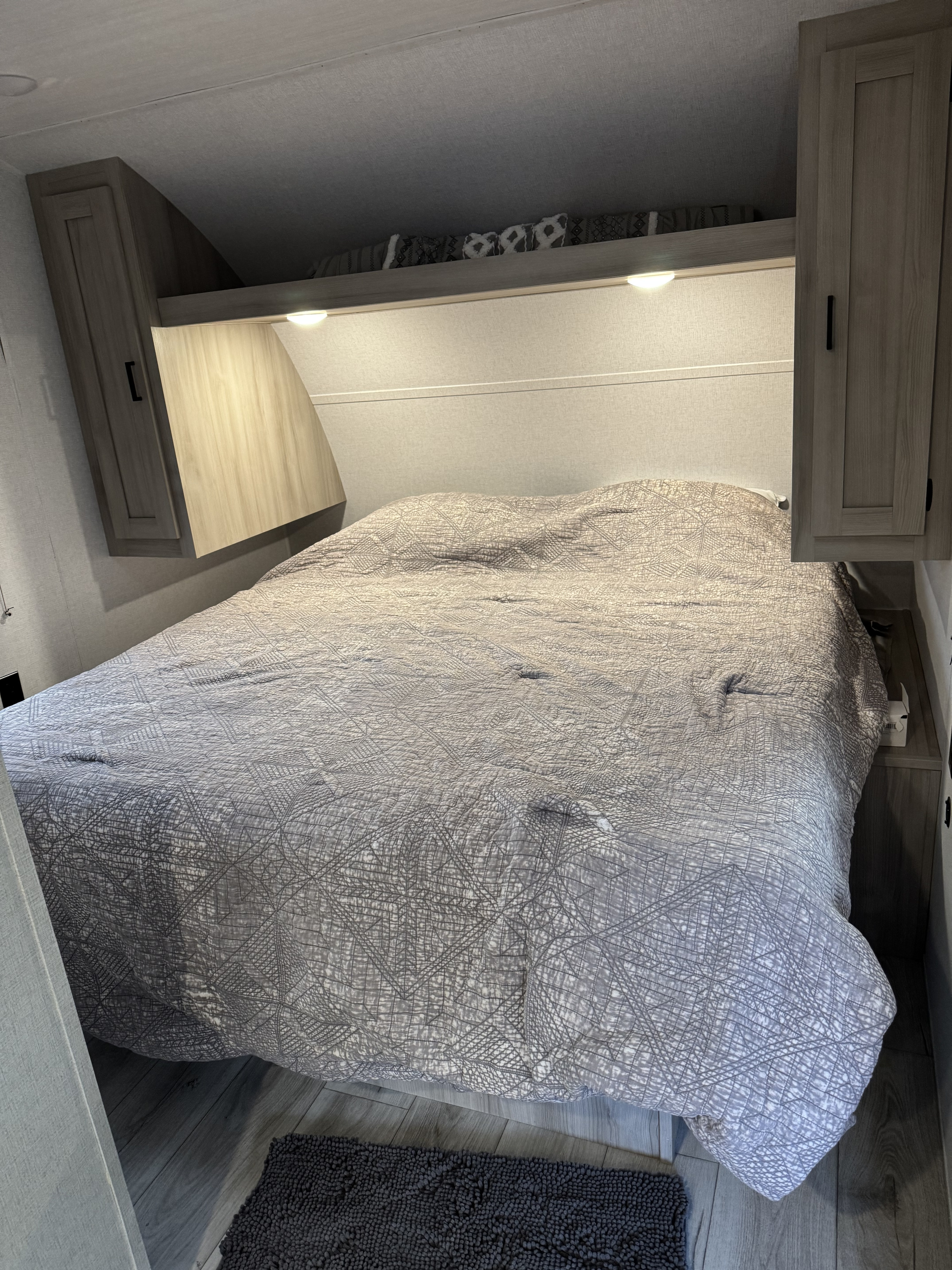Cozy RV rental bedroom, with a neatly made bed, patterned comforter, overhead cabinets, and reading lights.. East to West Silver Lake 2024