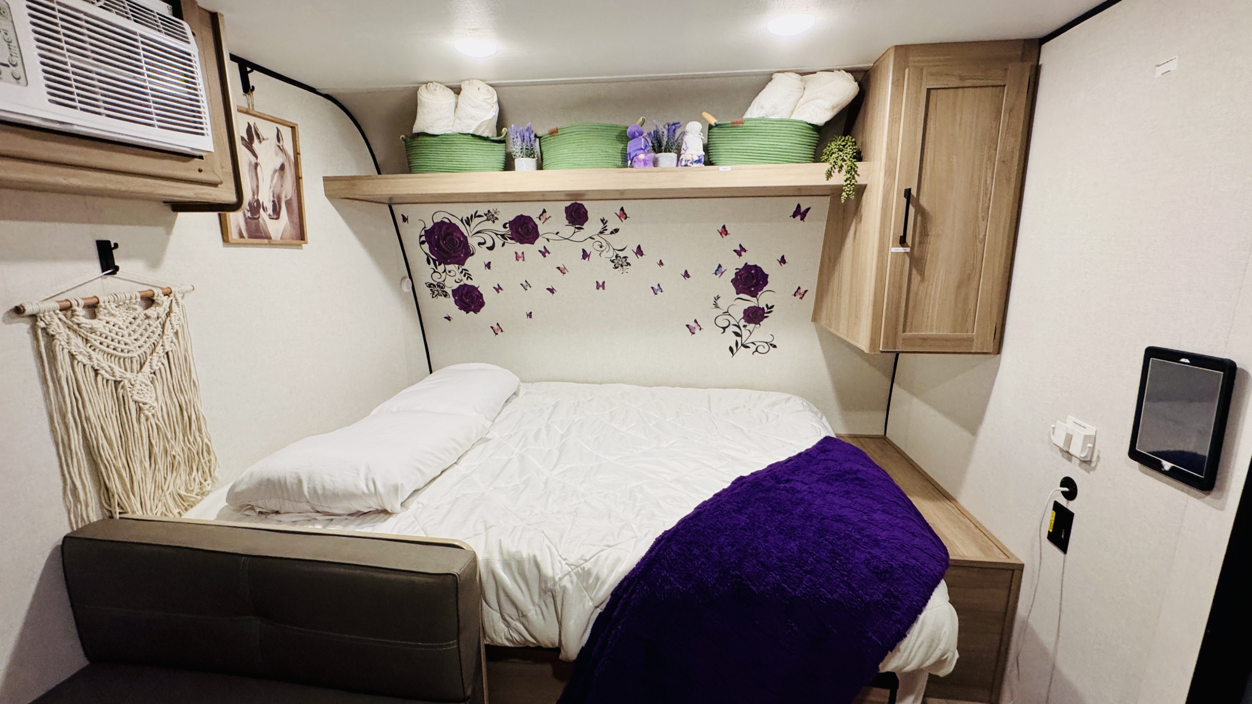 Inviting RV rental sleeping area features a bed with purple throw, butterfly decals, AC, and handy tech.. Keystone RV Coleman 2024