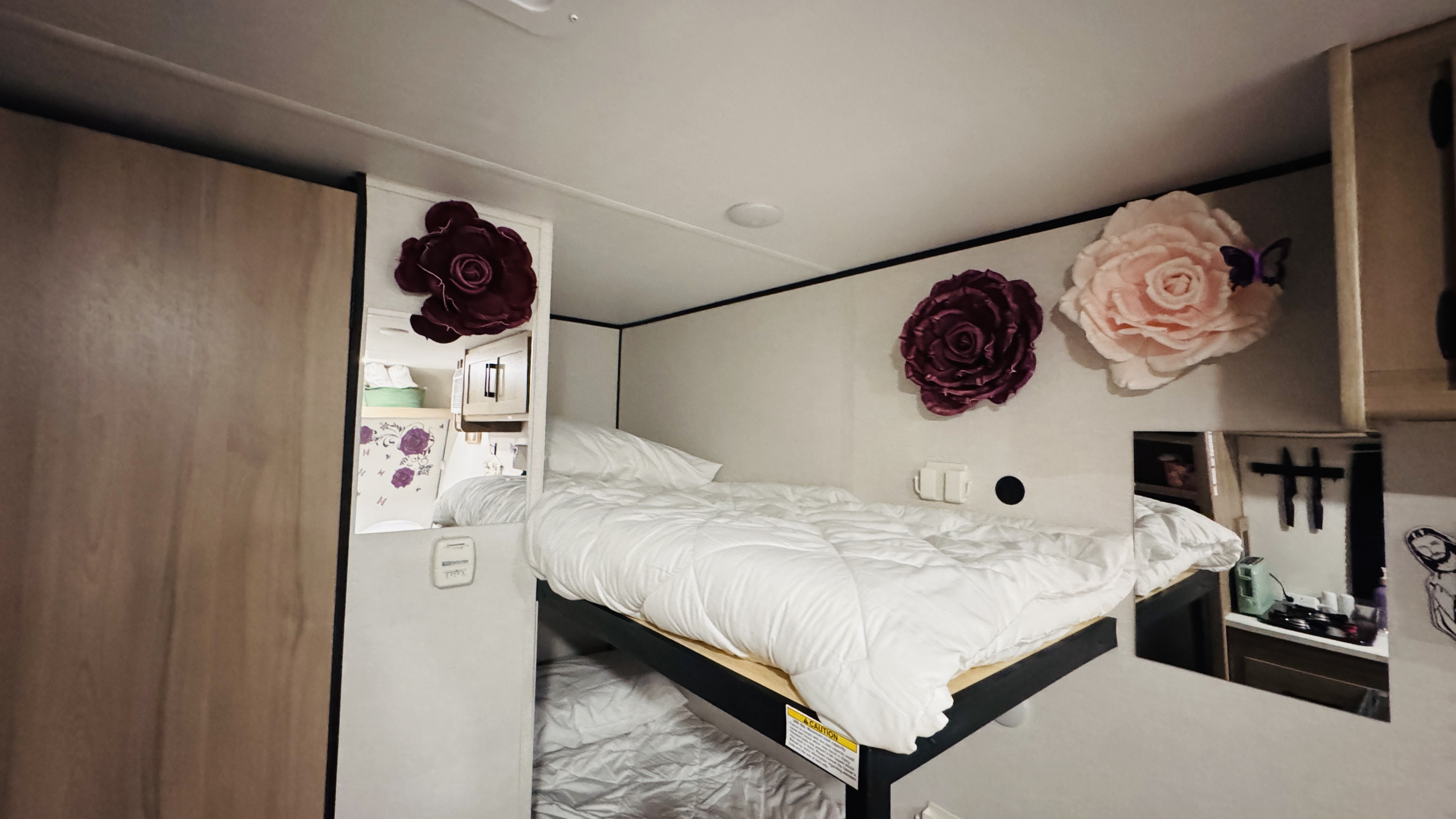 Cozy bunk beds in an RV rental, adorned with decorative flowers. Mirrored surfaces show a compact kitchen area.. Keystone RV Coleman 2024