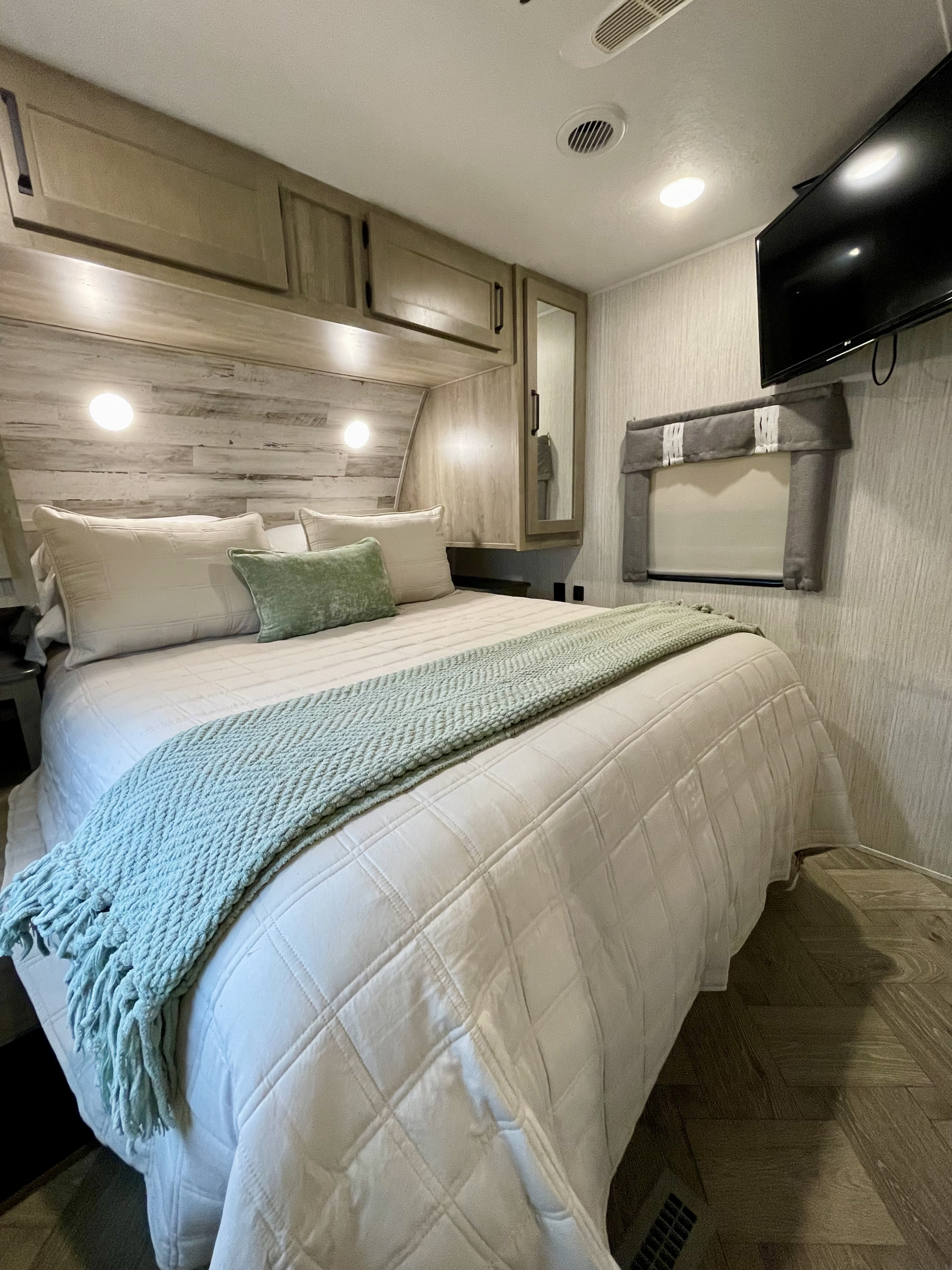 This modern RV rental bedroom offers a comfortable bed with white & green decor, built-in storage, a TV, and wood-look floors.. Forest River Palomino Puma 2022