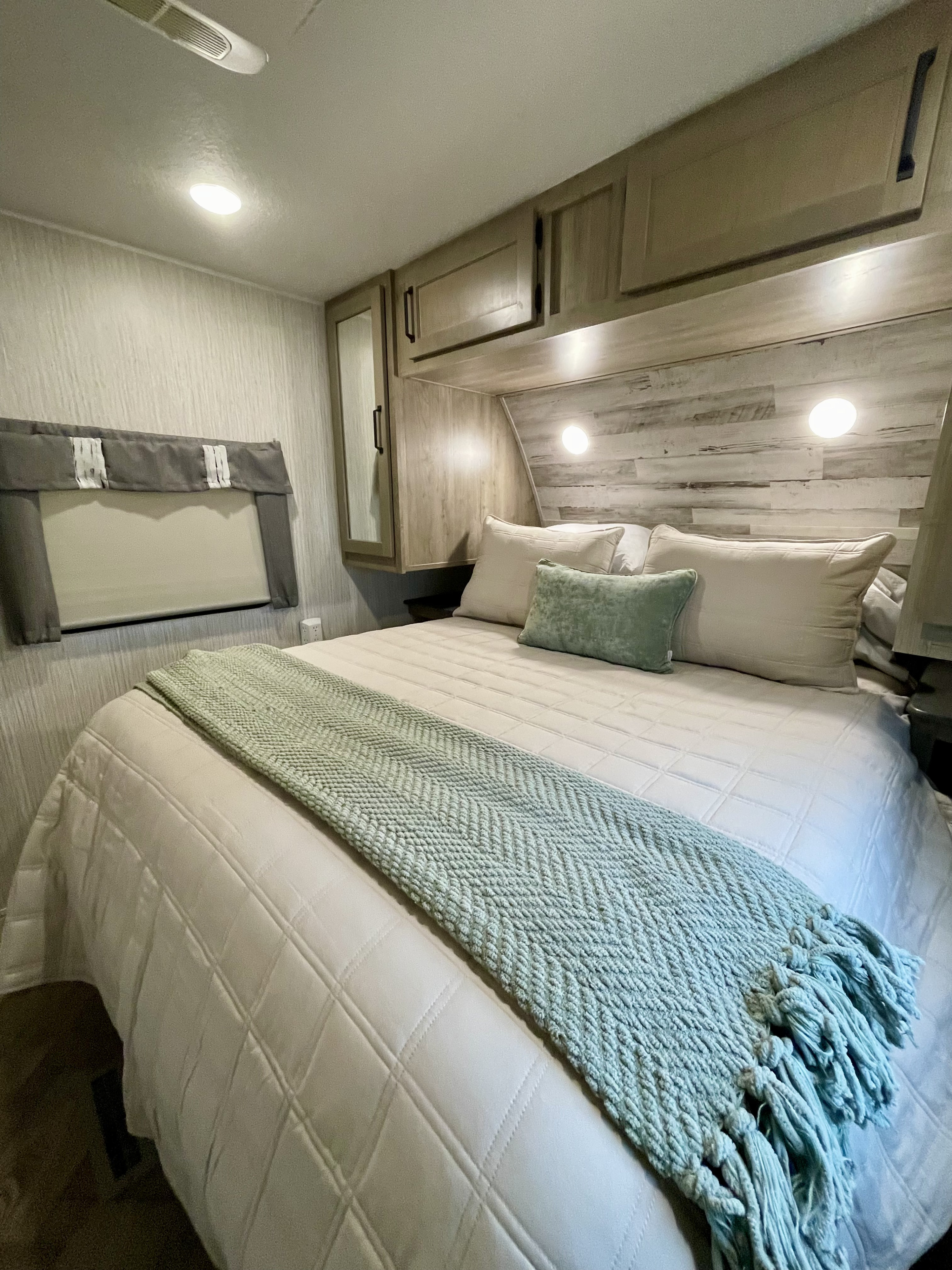 Cozy RV rental bedroom with a comfy bed, quilted bedding, and a decorative green throw, illuminated by bedside lights and overhead storage.. Forest River Palomino Puma 2022