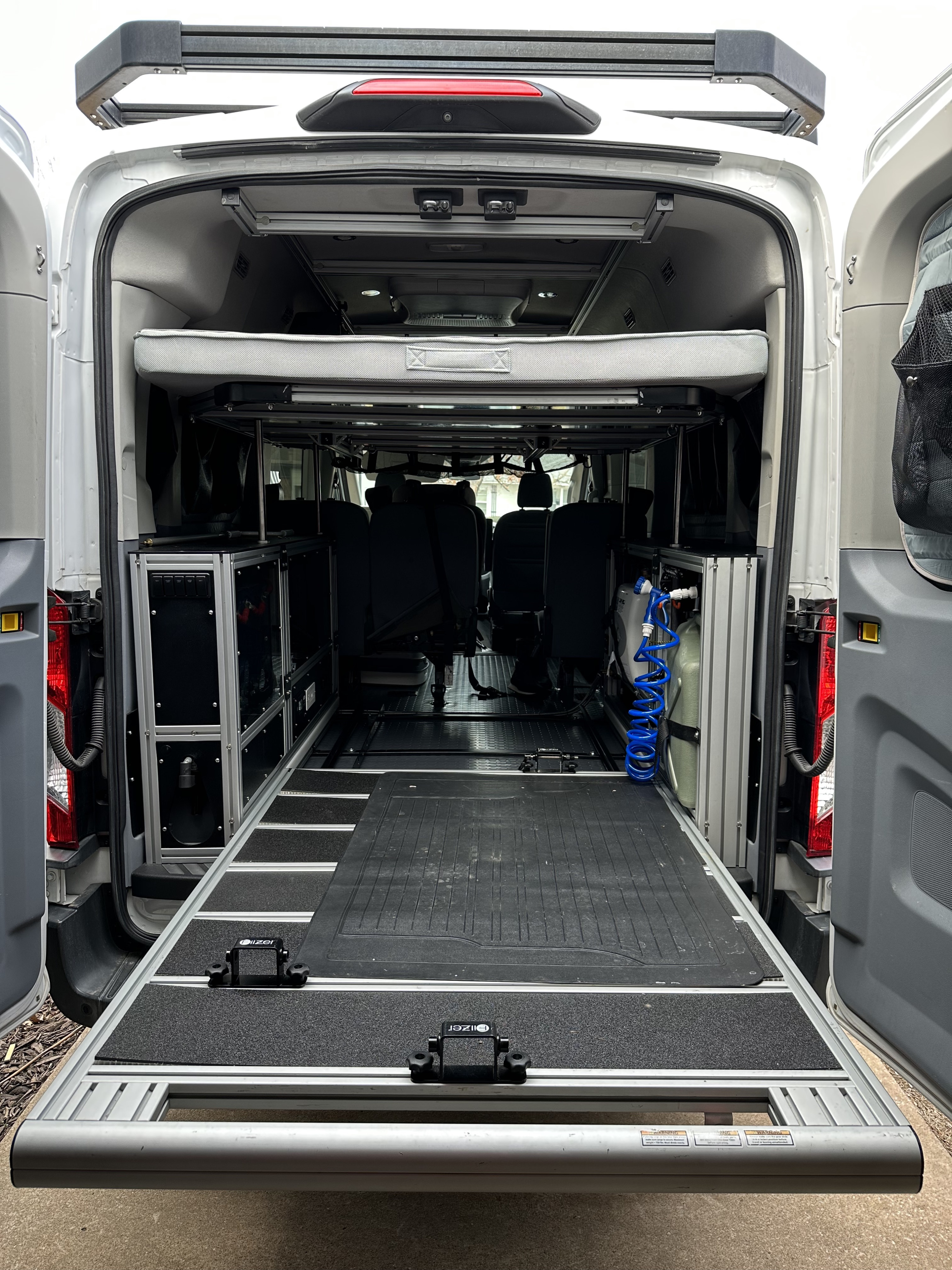 Rear view of an RV rental camper van showing a pull-out cargo slide, overhead bed, and integrated storage units.. Ford Transit 2018