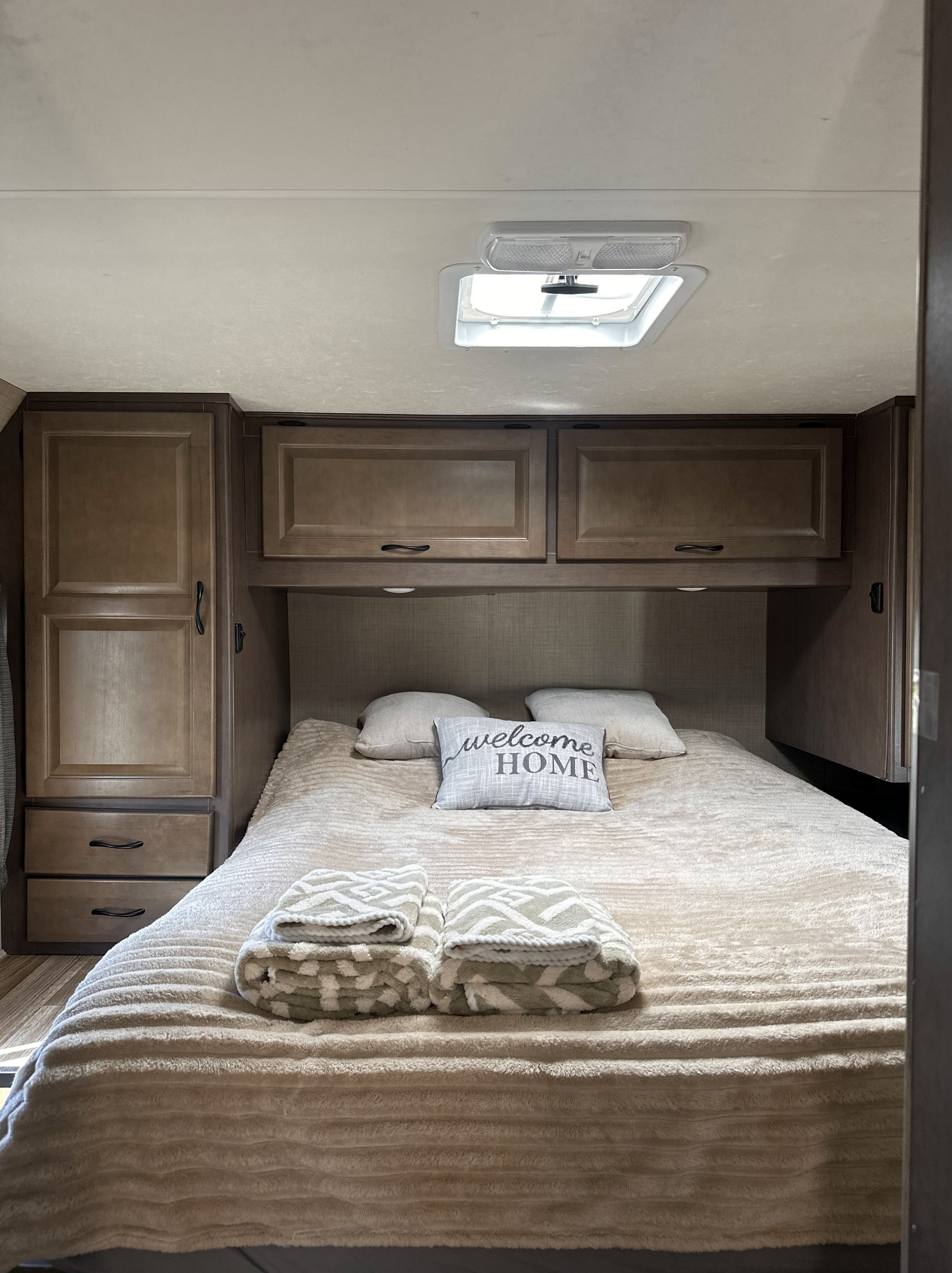 Cozy RV rental bedroom with a plush bed, "welcome HOME" pillow, wood cabinets, and a ceiling vent. Ready for your trip.. Thor Majestic 2020