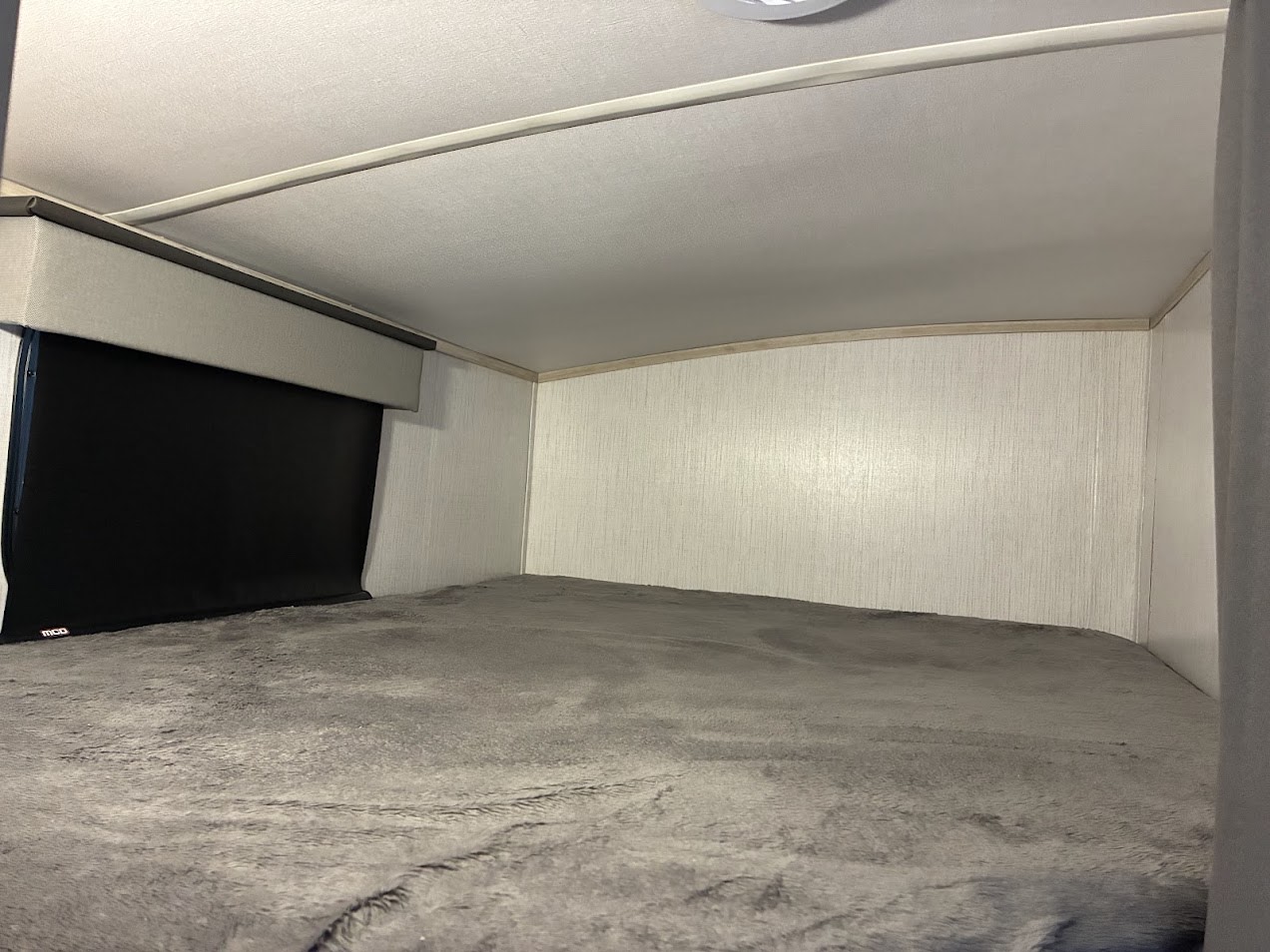 Inside an RV rental: a gray, plush bunk bed with a pulled-down window shade, offering a cozy sleeping area.. Twilight RVS Signature 2022