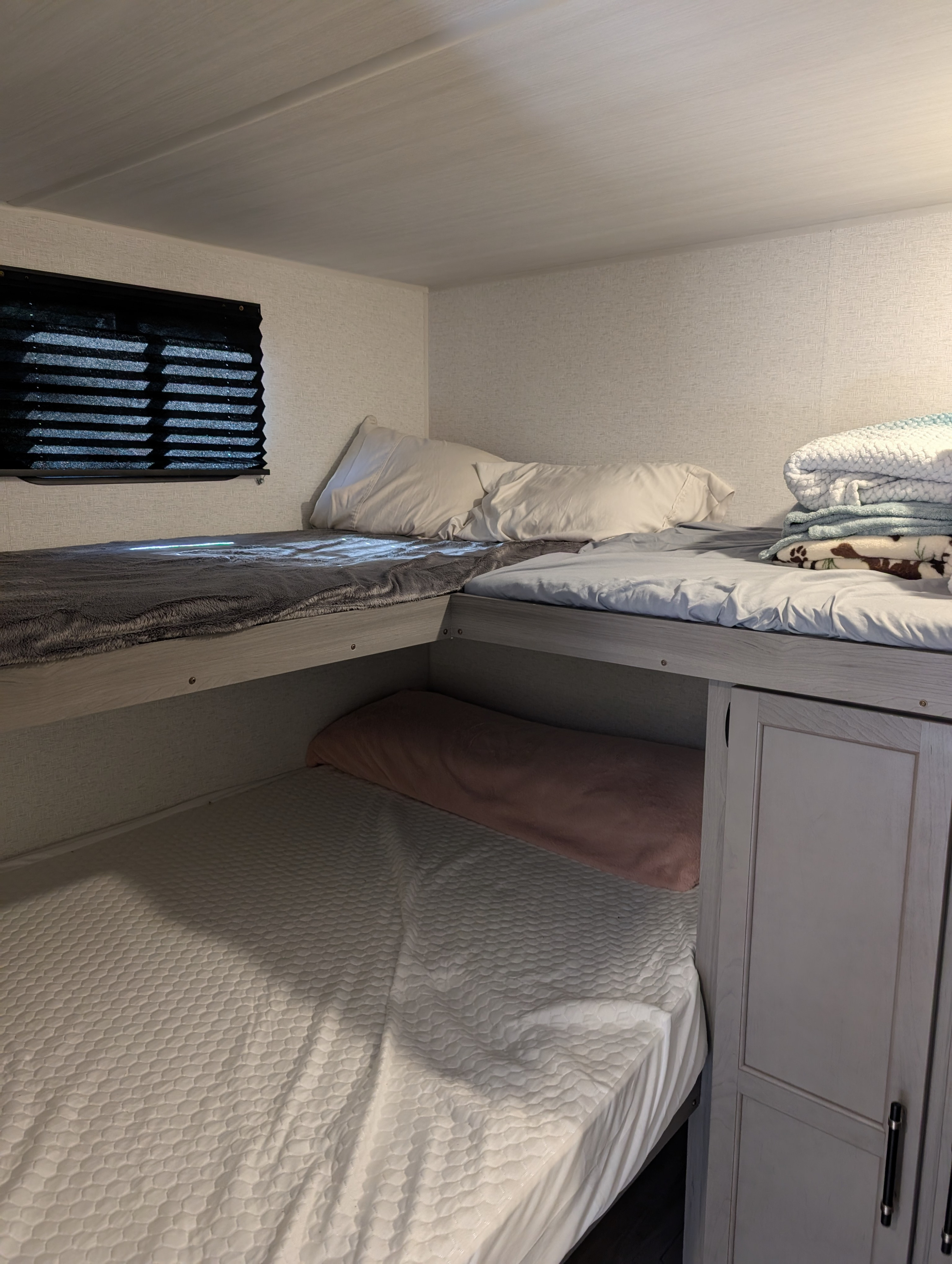Inside an rv rental: a compact sleeping area with two comfy bunk beds, pillows, blankets, window blinds, and storage.. Keystone RV Hideout 2025