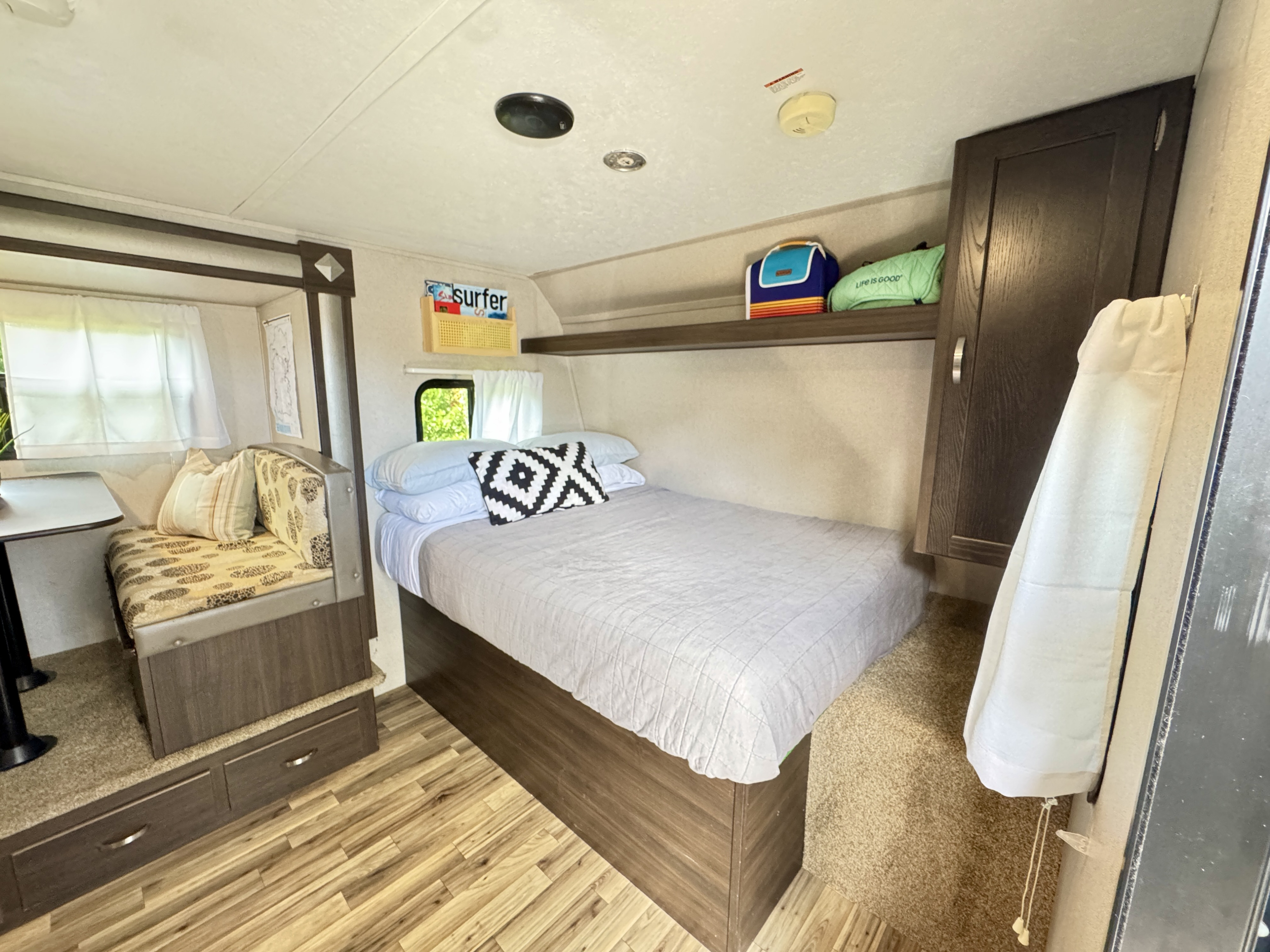 RV rental interior showcases a comfy bed, small dinette with storage, wood-look flooring, and ceiling details.. Keystone RV Springdale 2019